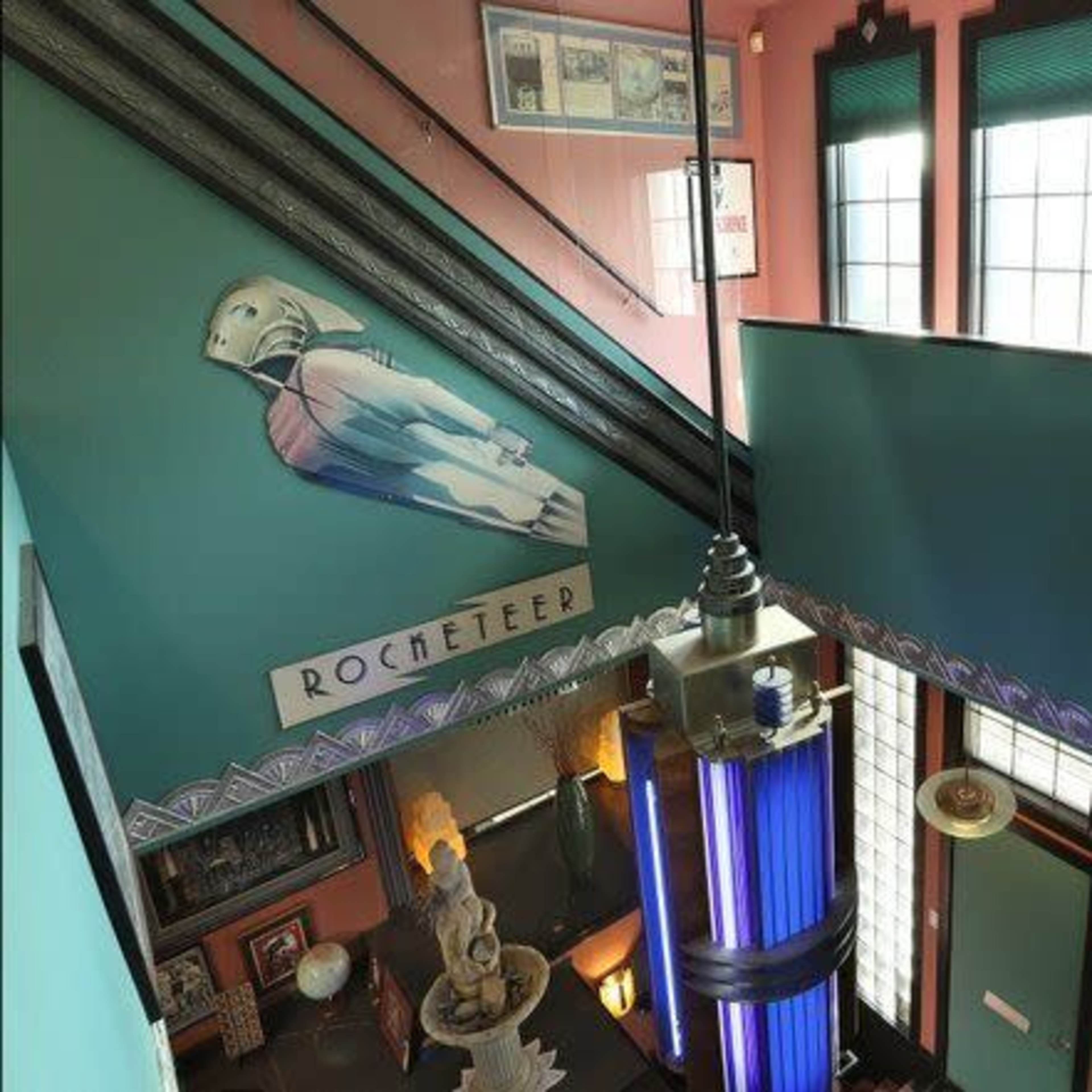 A staircase area featuring vintage décor, including a Rochette-themed mural on the wall and a colorful light fixture overhead.