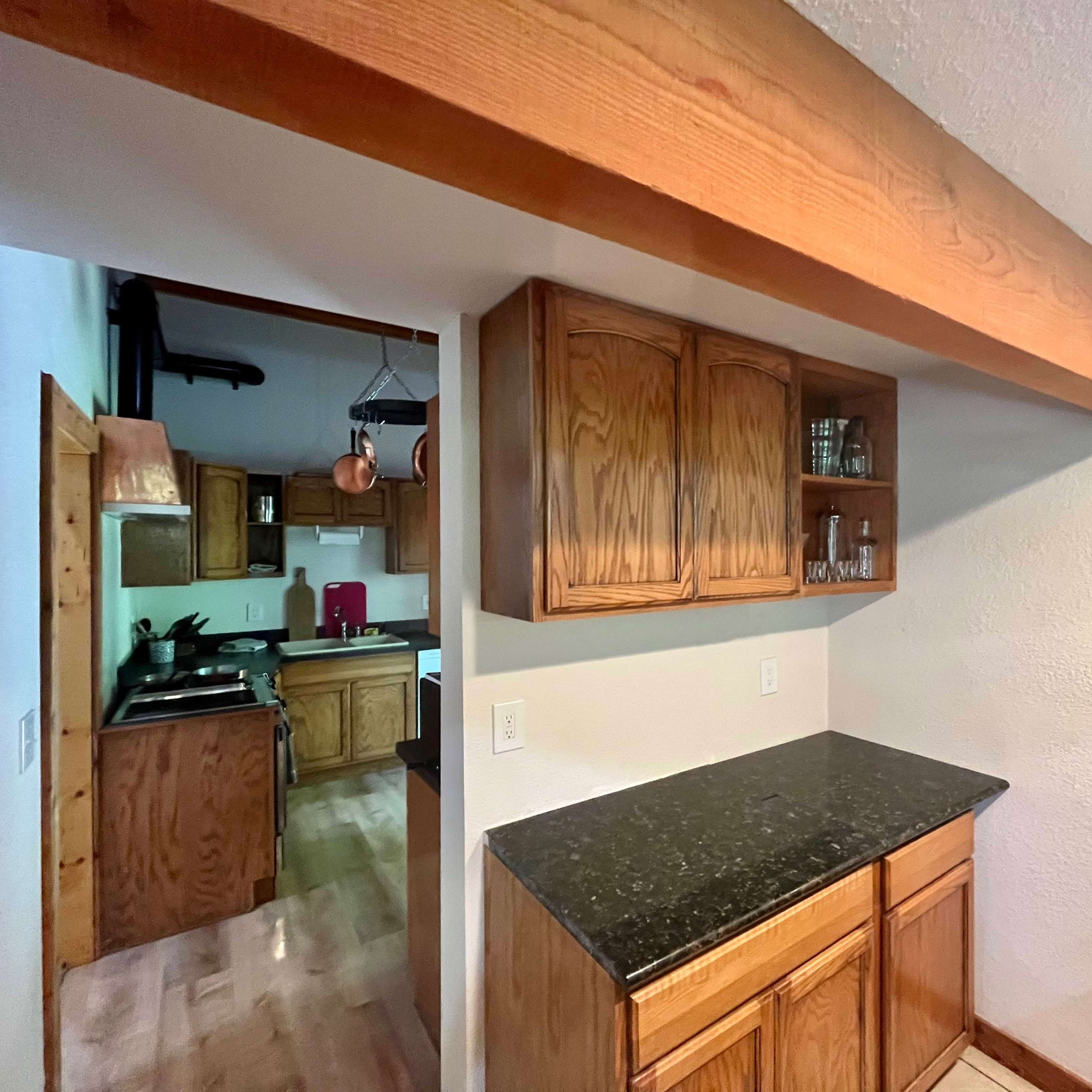 A kitchen area featuring wooden cabinets, a granite countertop, and a visible hallway leading to another section of the kitchen.