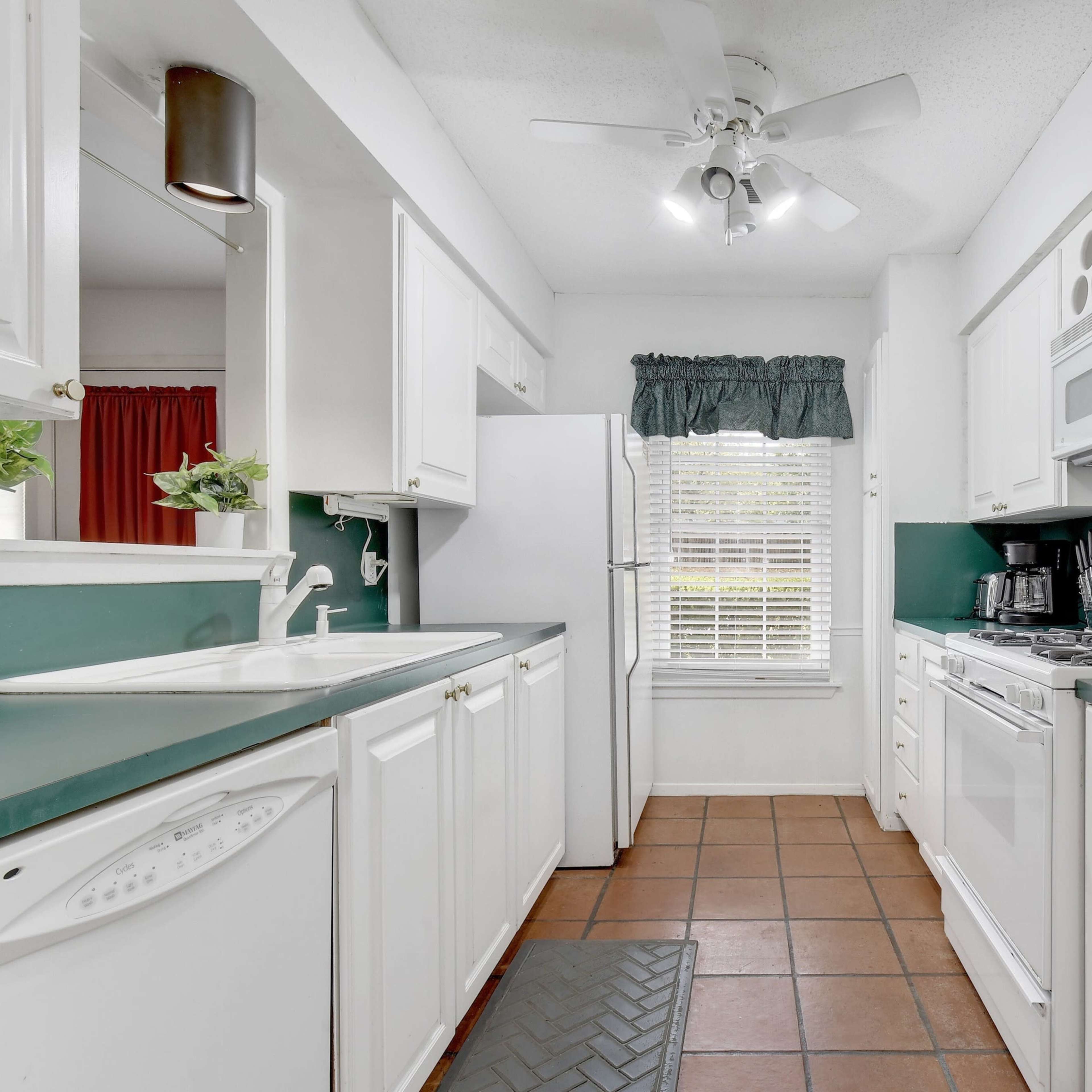 A compact kitchen with white cabinetry, green countertops, and a window letting in natural light.