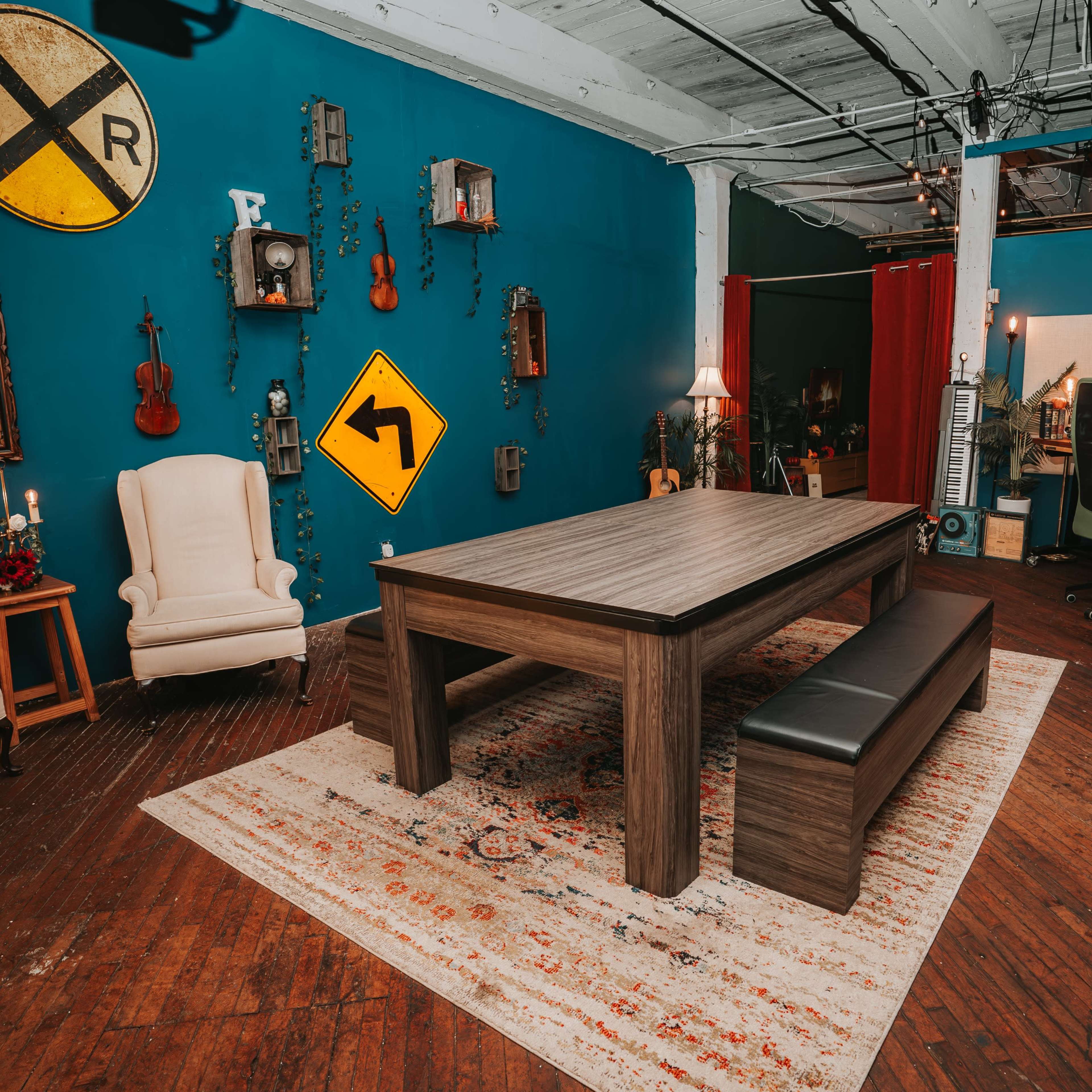 A spacious room with a central wooden table surrounded by benches, decorated with various musical instruments, wall art, and traffic signs against a vibrant blue background.