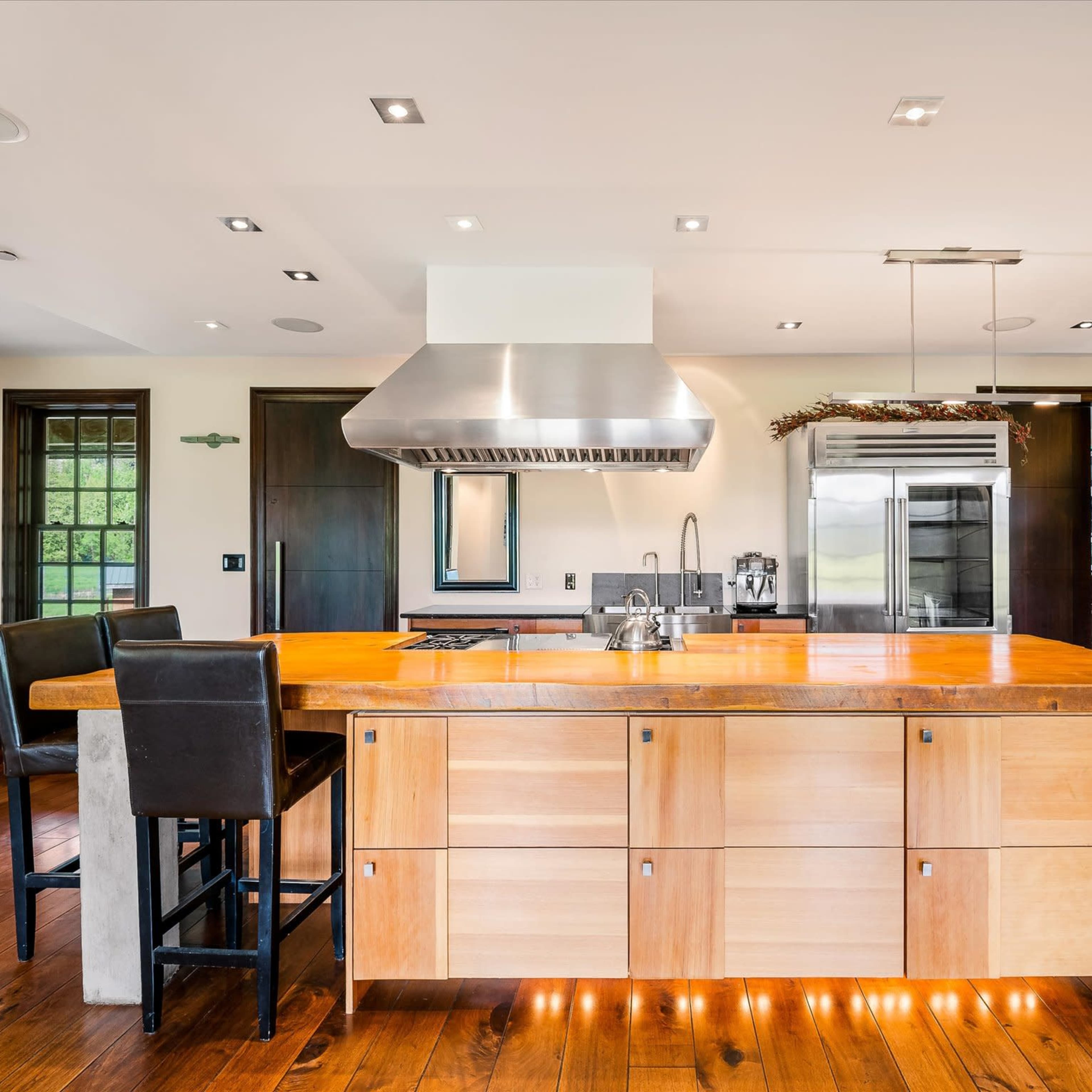 A modern kitchen featuring a central island with a wooden countertop and a stainless steel range hood above a gas stove.