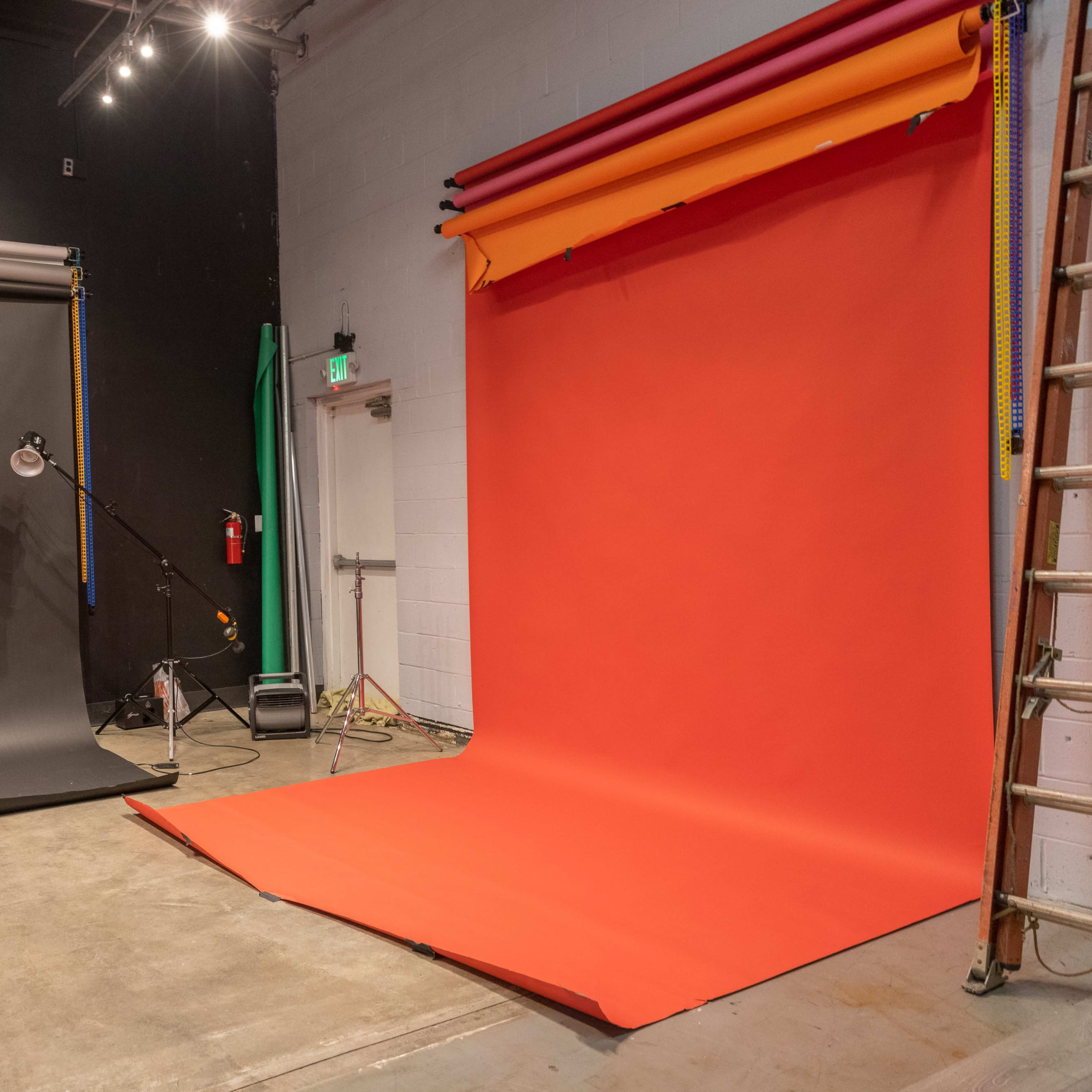 A photography studio with two backdrops, one black and one bright red, along with a clear chair and various equipment visible on the floor.