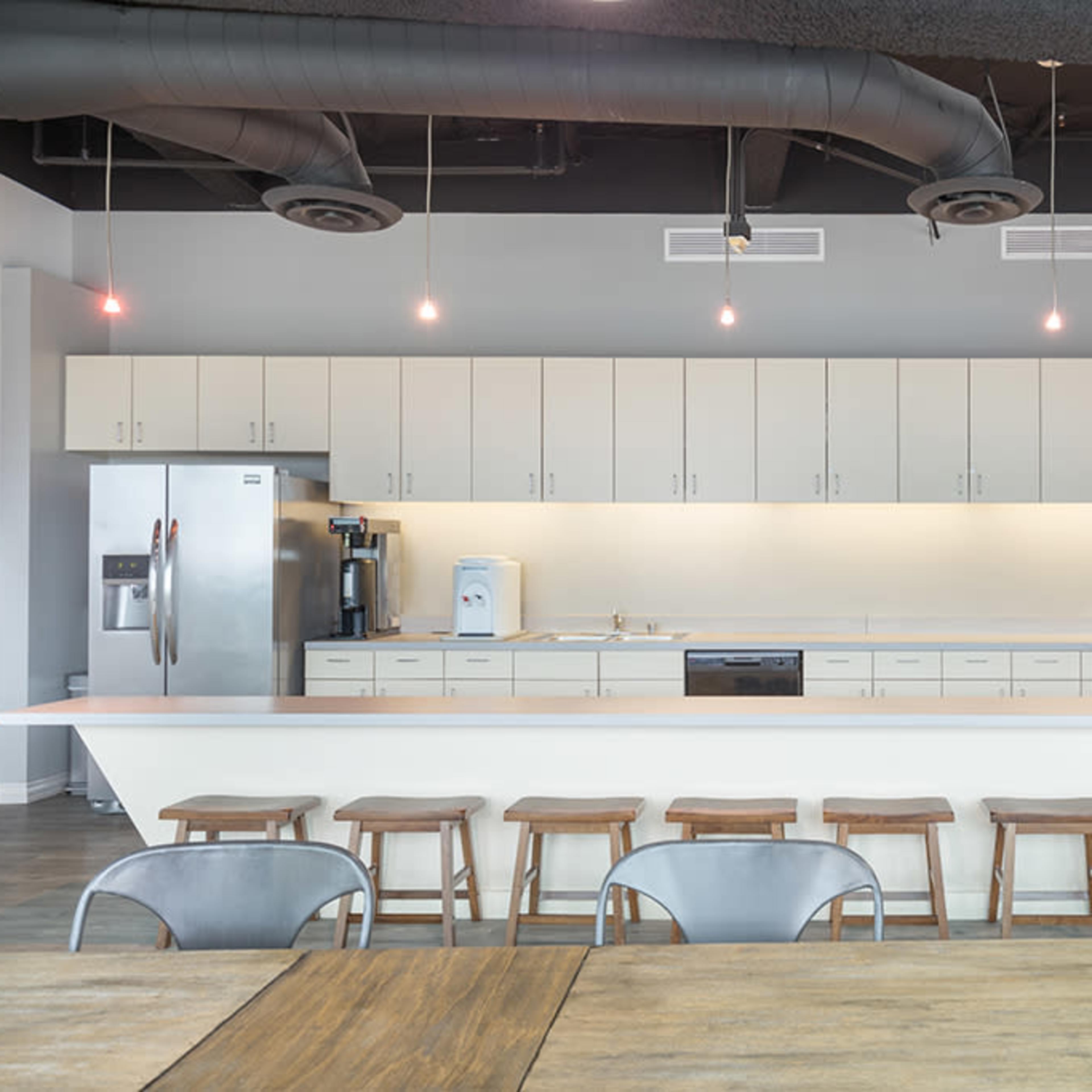 A modern kitchen area with a long countertop, several stools, and an array of cabinets above and below.