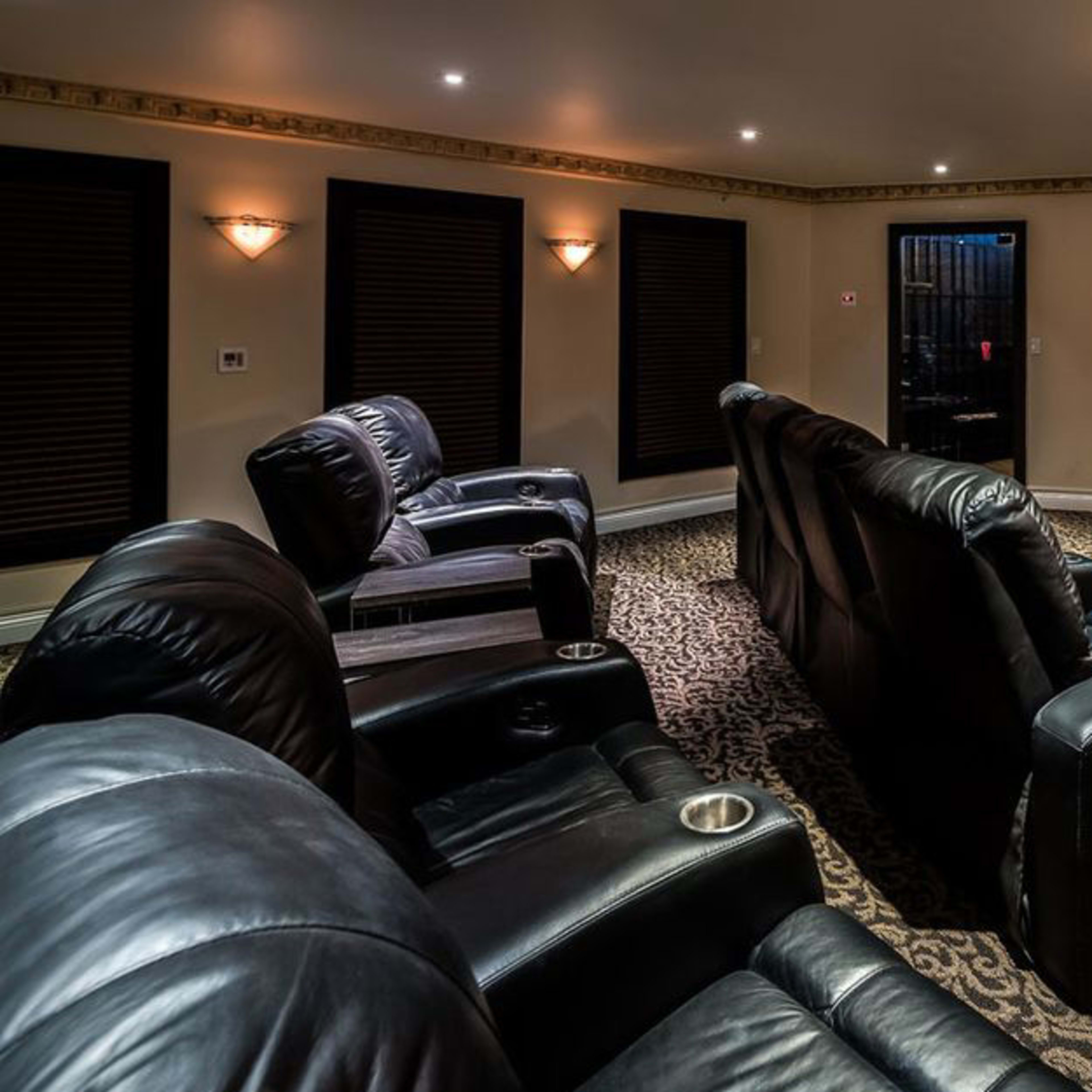 A dimly lit home theater featuring black leather recliners and a large screen displaying a movie.