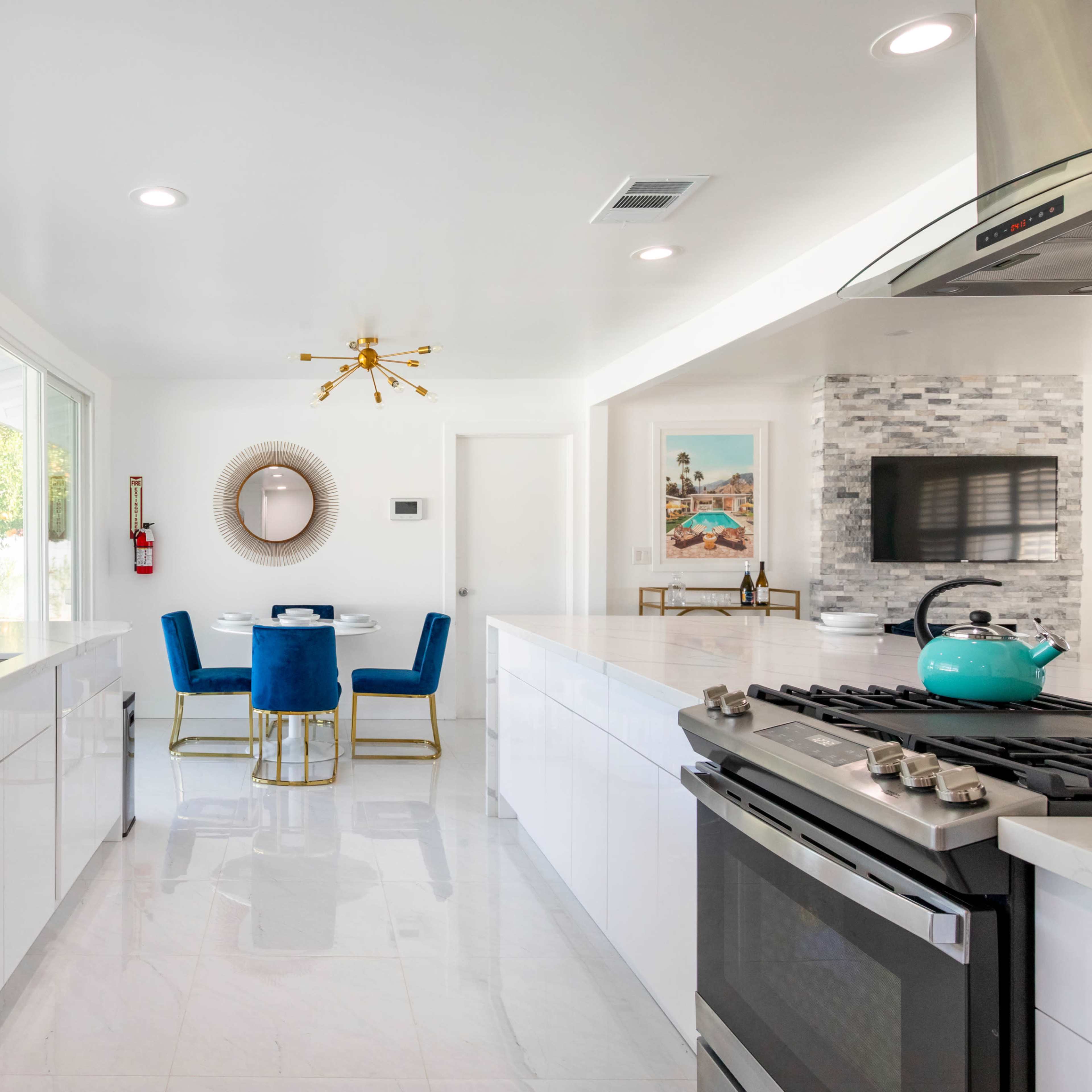 A modern kitchen and dining area with white cabinets, a stainless steel stove, and a small round dining table surrounded by blue chairs.