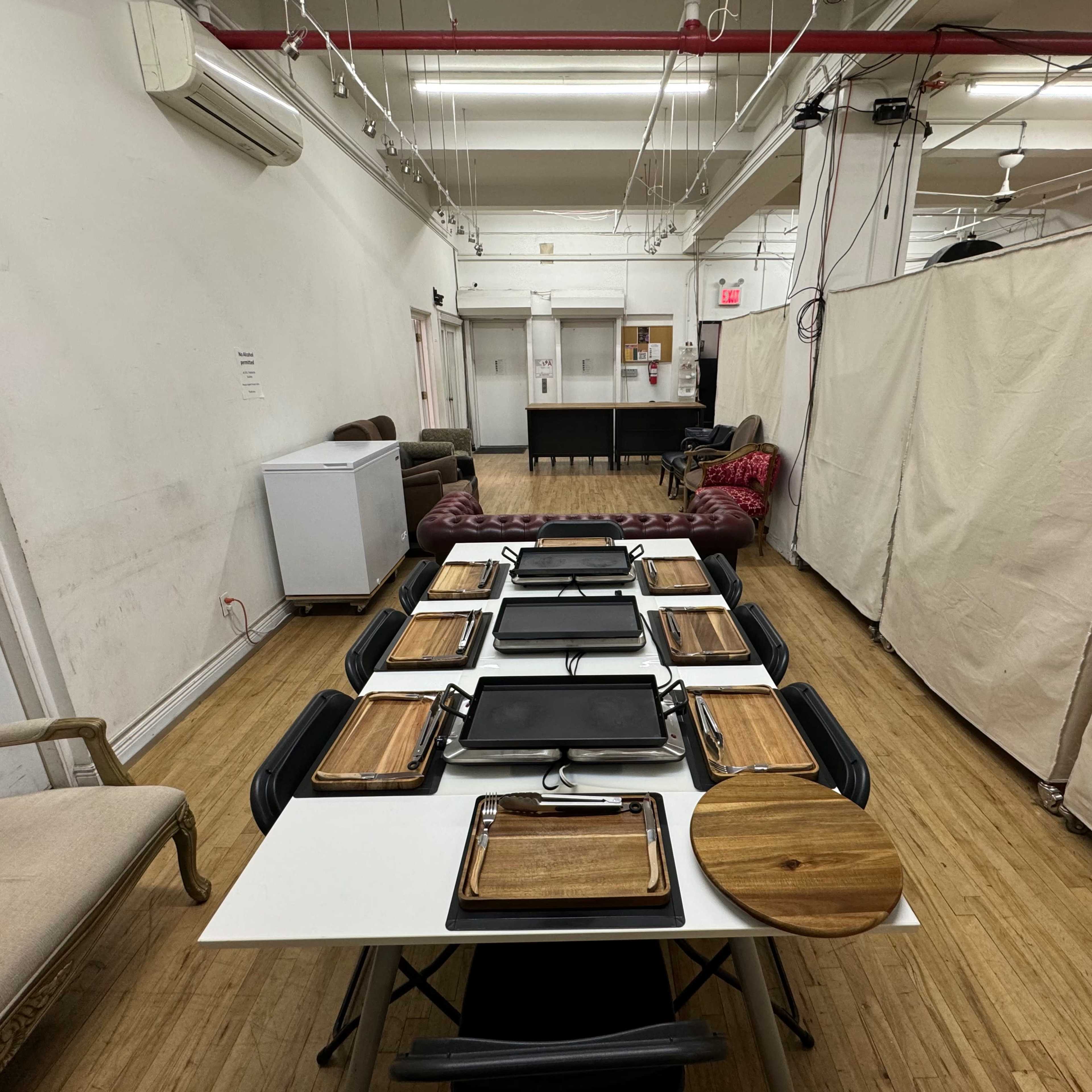 A long table is set up with several grilling trays and wooden serving platters in a spacious, minimalist room.