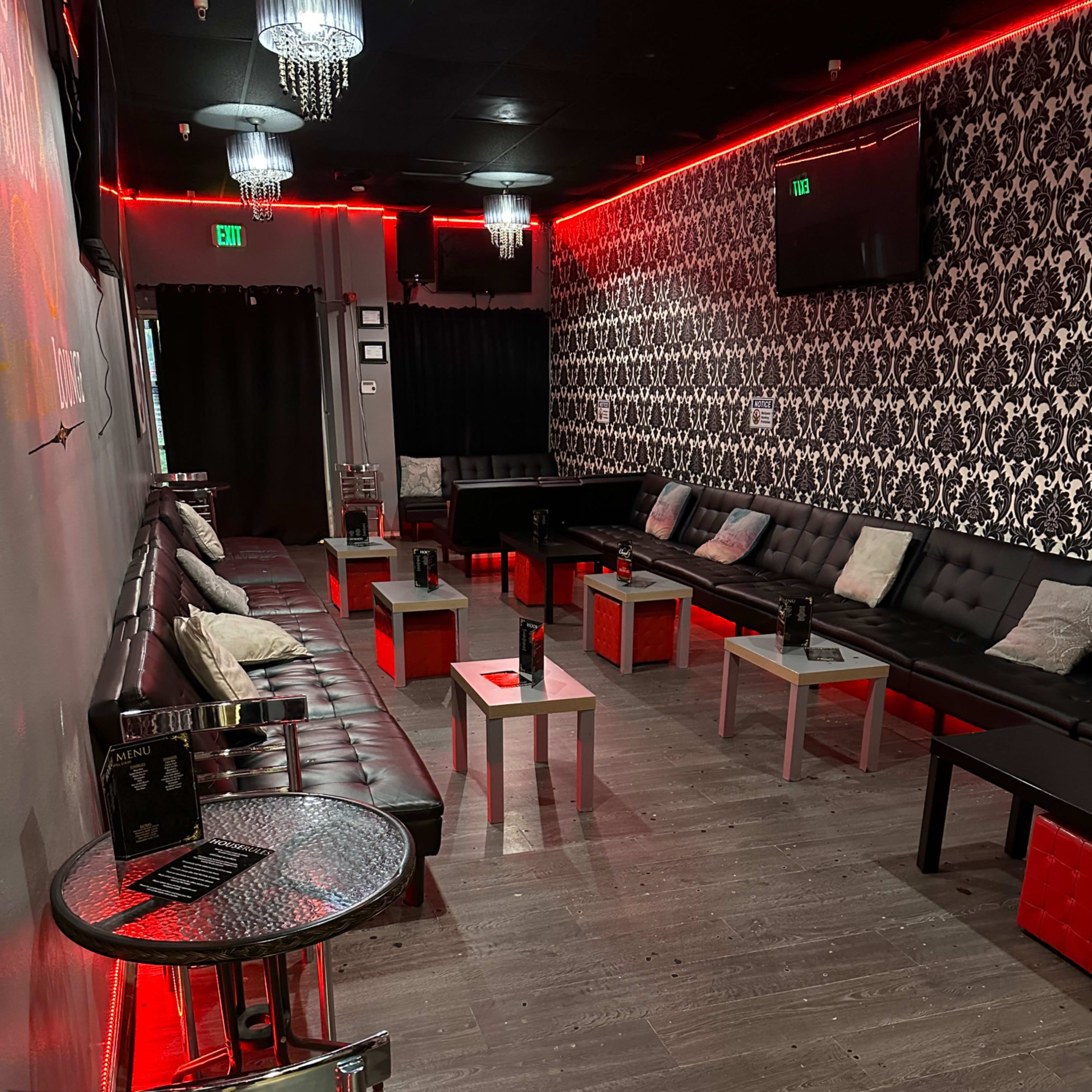 A dimly lit lounge area with black leather seating, small tables, and red accent lighting.