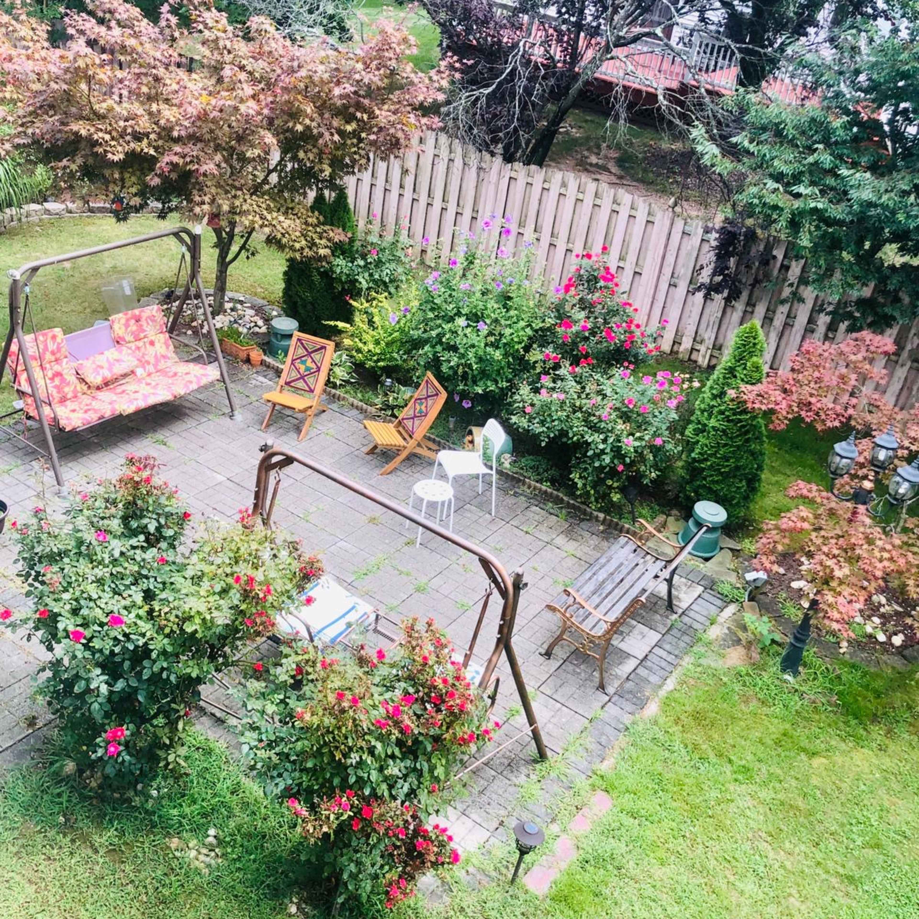 A landscaped garden with floral shrubs, a swing set, and various pieces of garden furniture arranged on a stone patio.