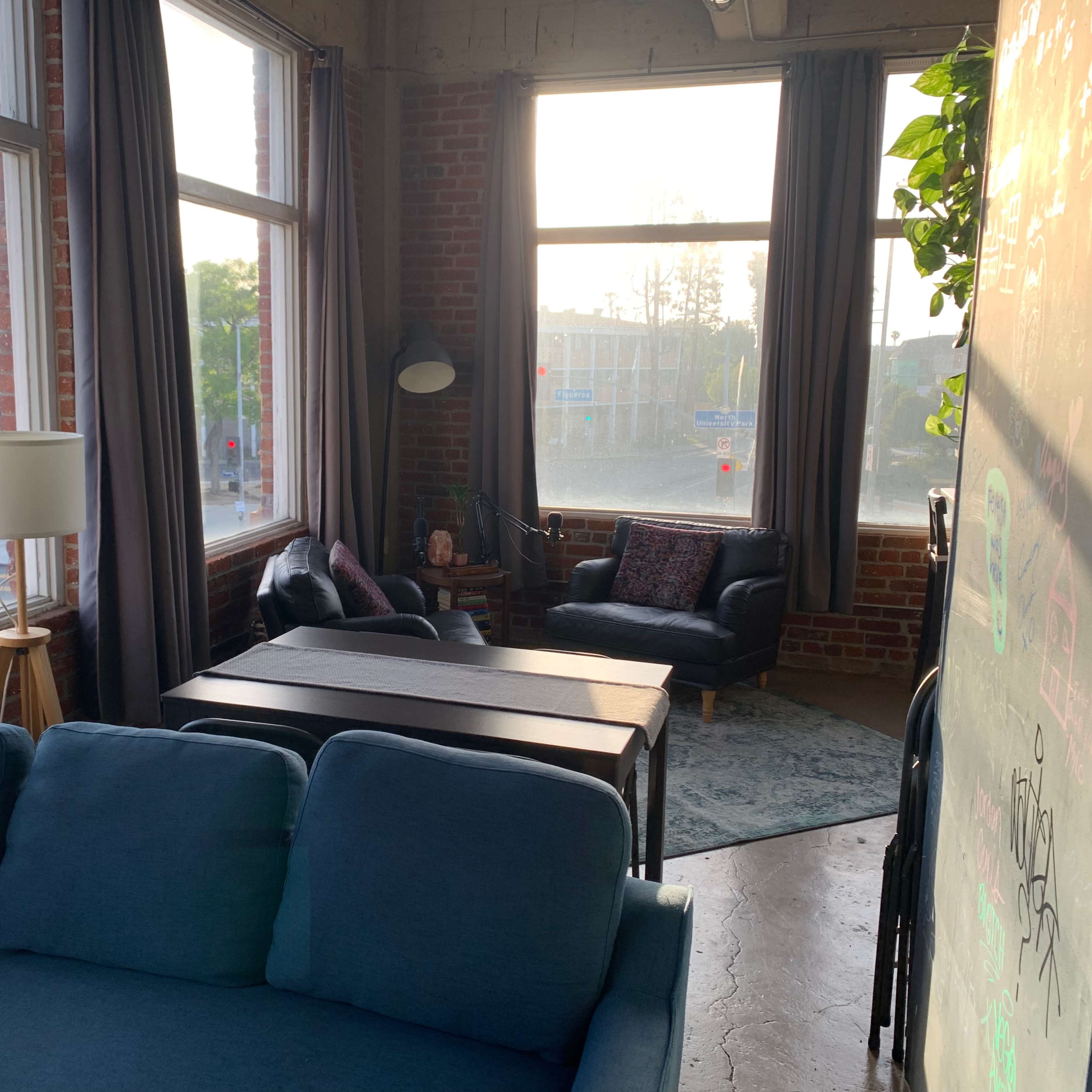 A cozy living space with large windows, a blue sofa, a coffee table, and two leather chairs arranged near a floor lamp.