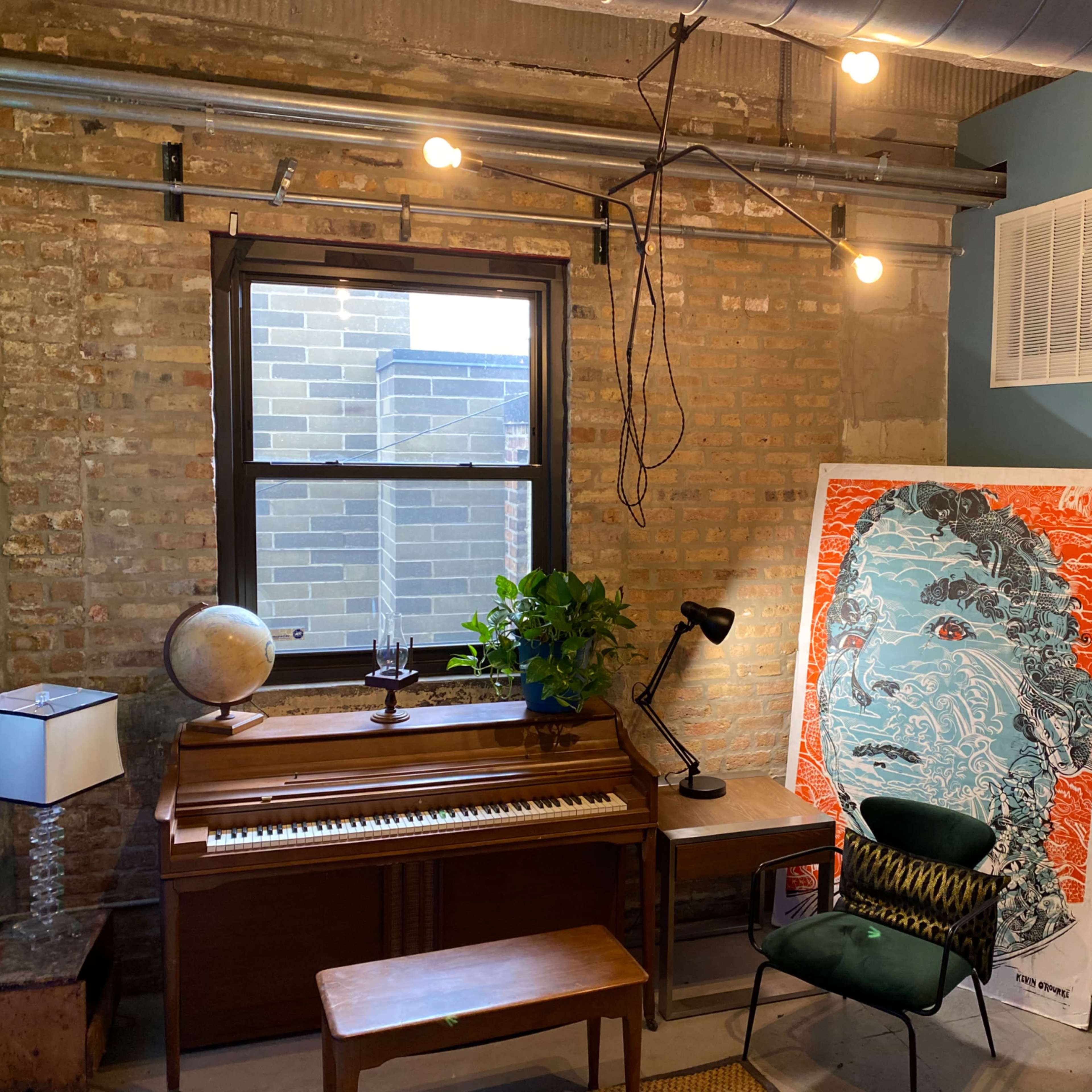 A cozy room featuring a piano, a globe, a potted plant, a modern floor lamp, and a colorful artwork on the wall next to a window.