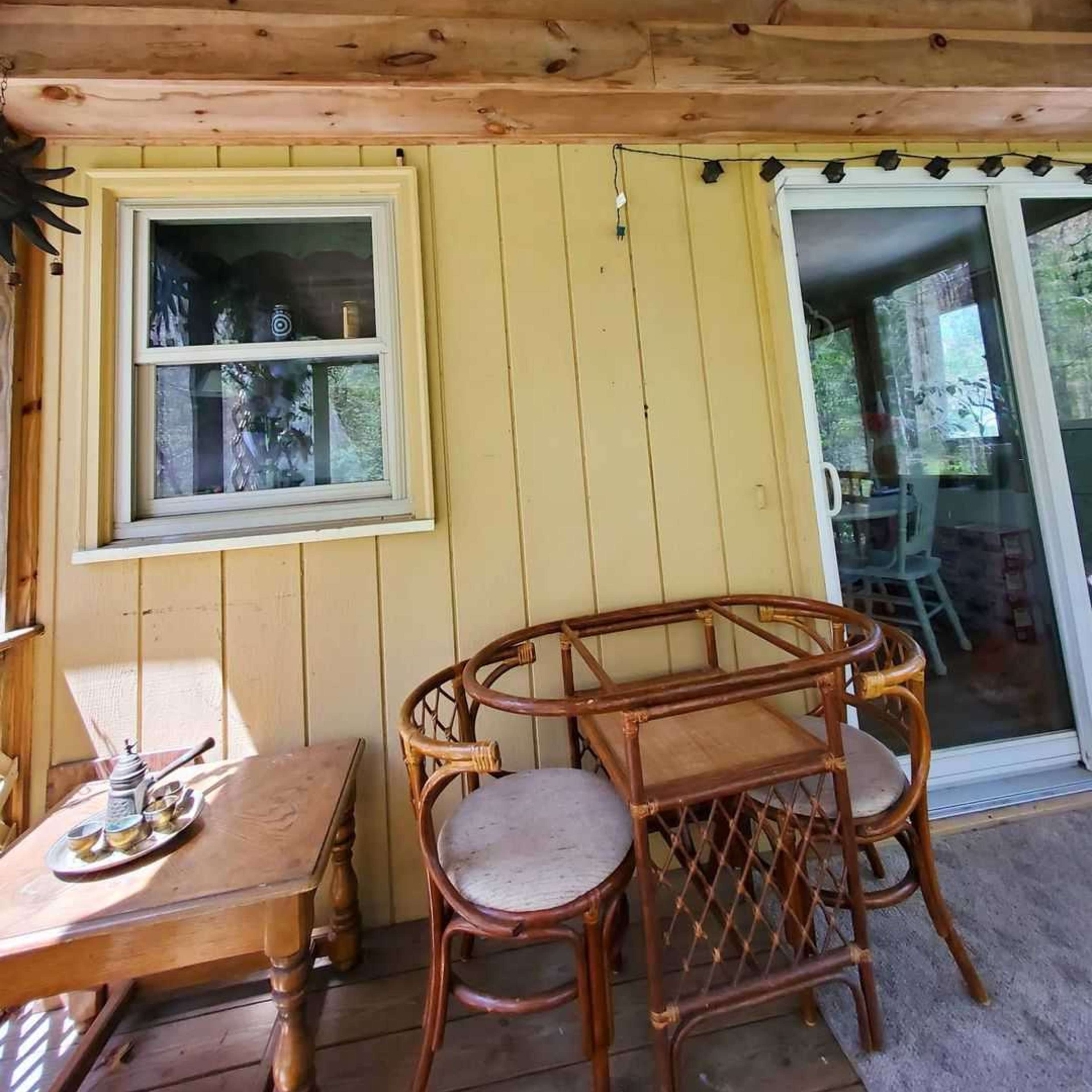 A small outdoor seating area with a round table and two chairs, adjacent to a yellow wooden wall and a sliding glass door.