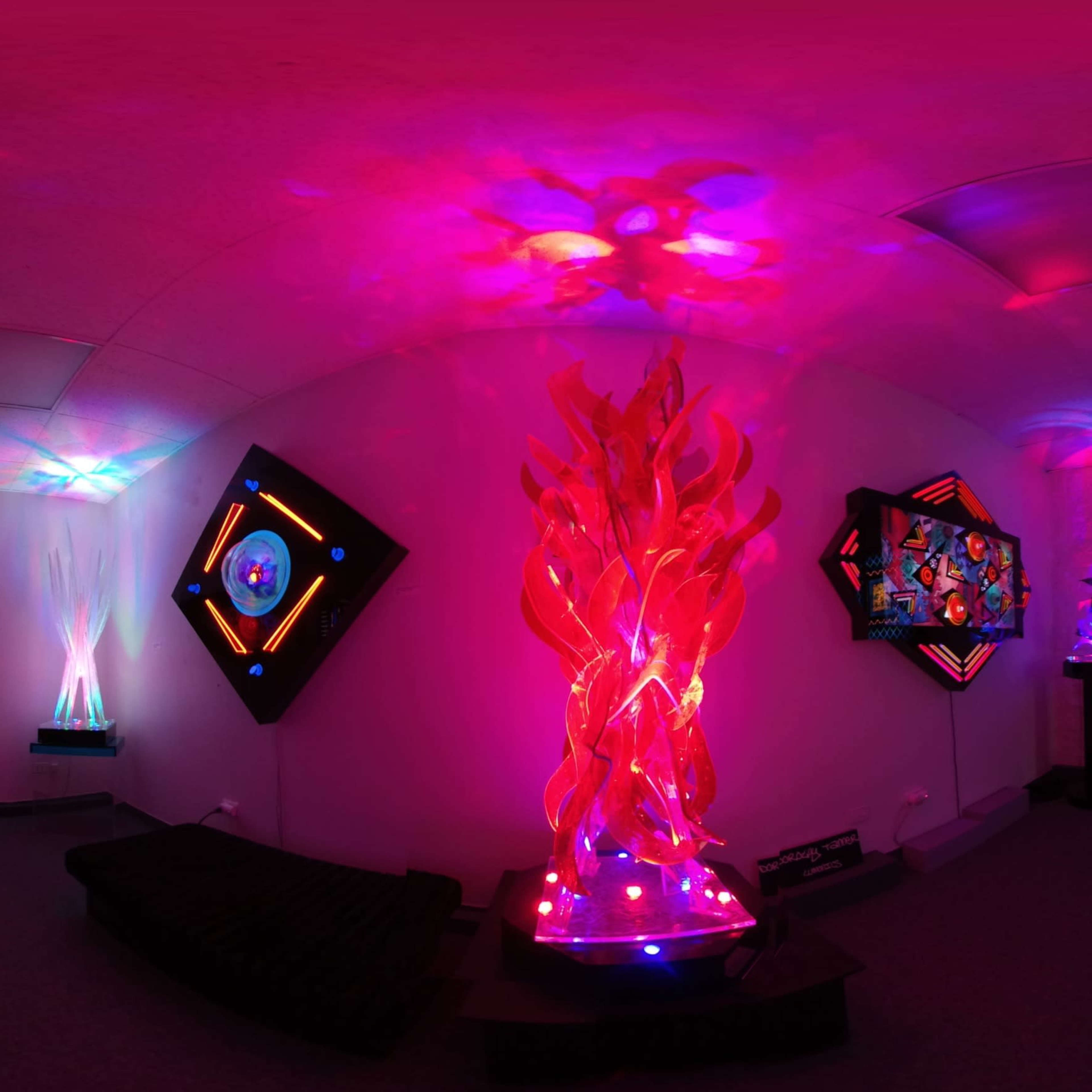 A vibrant art installation featuring colorful illuminated sculptures and wall art in a dimly lit room.