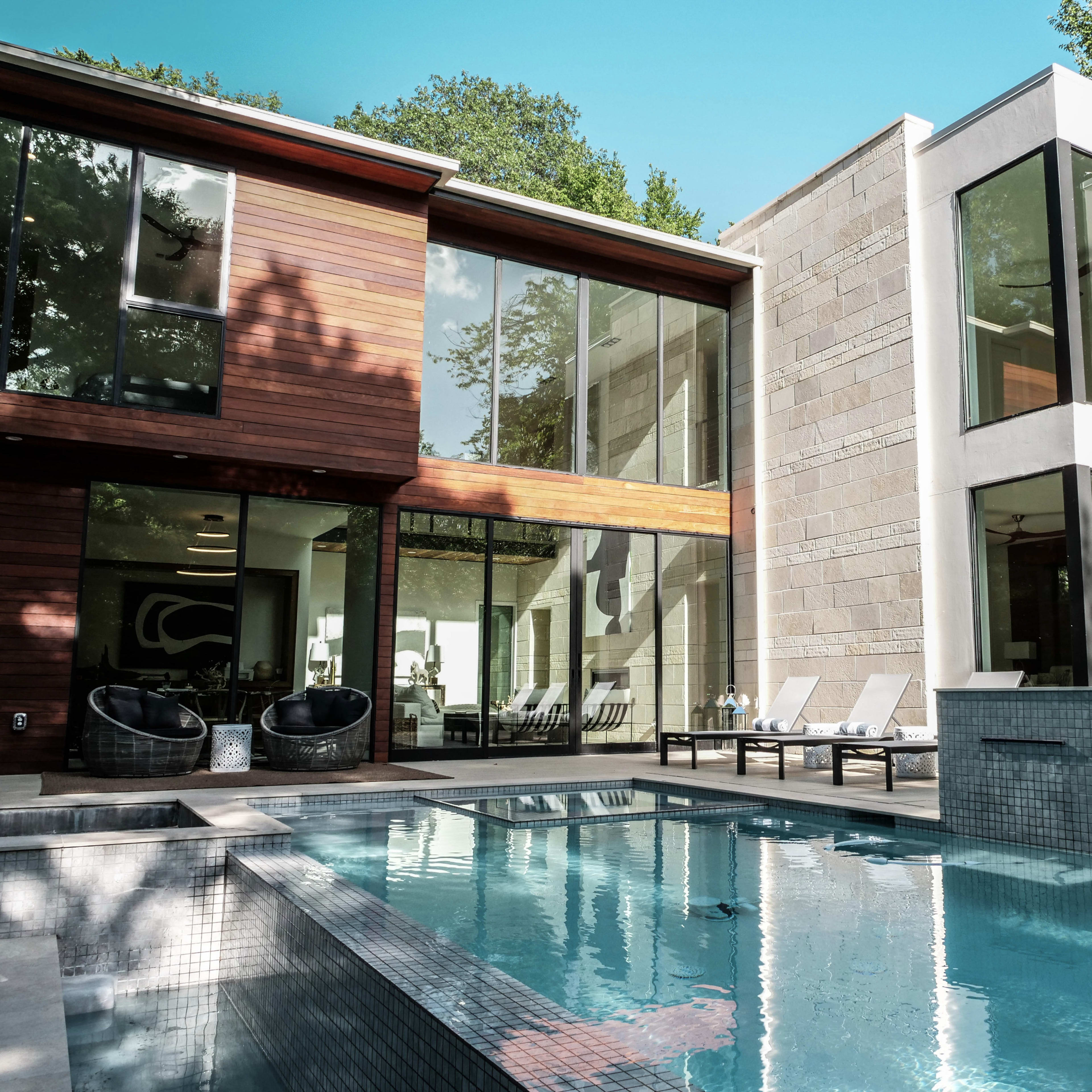 A modern house with large windows overlooks a rectangular swimming pool surrounded by lounge chairs.
