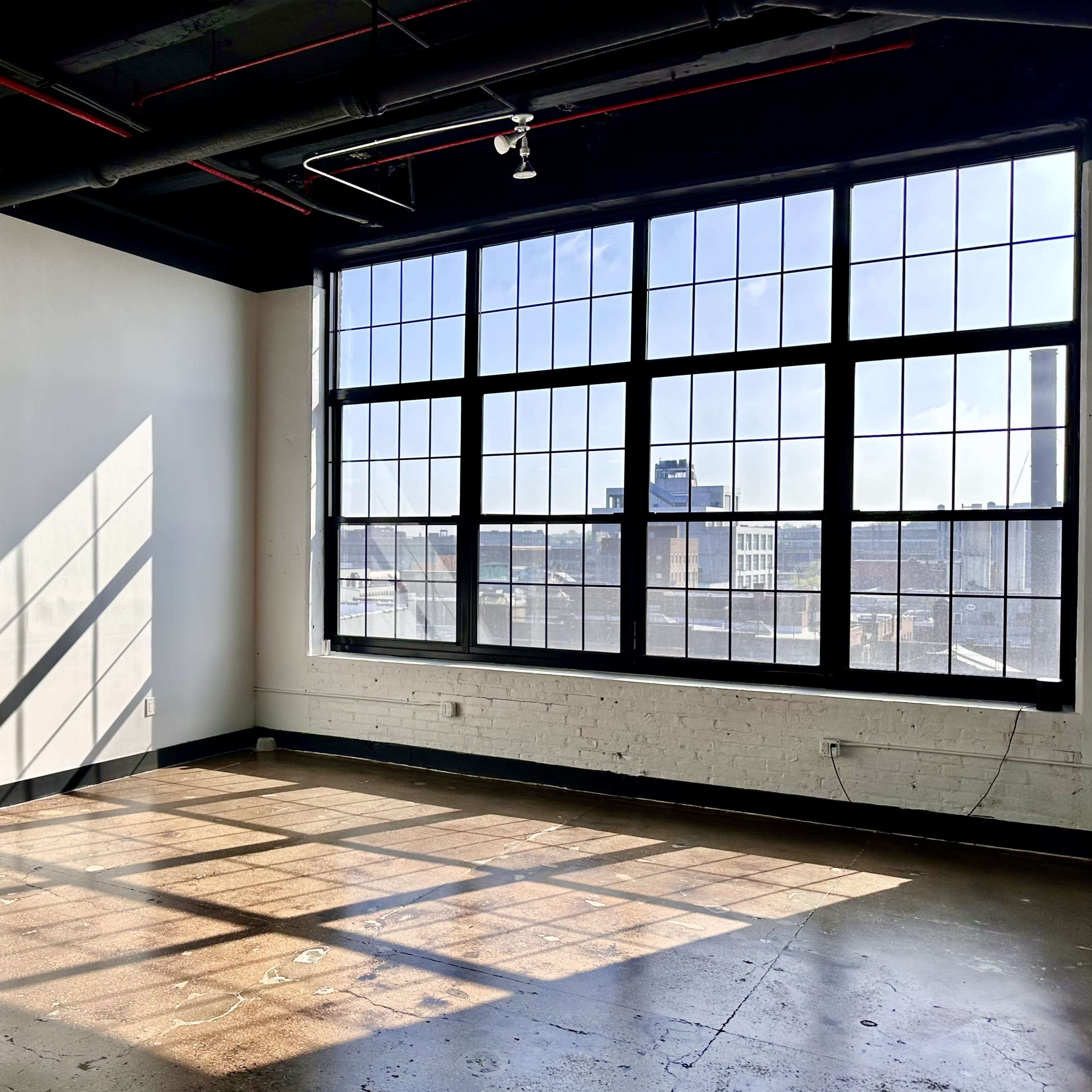 A sunlit room features large windows casting geometric shadows on the concrete floor.