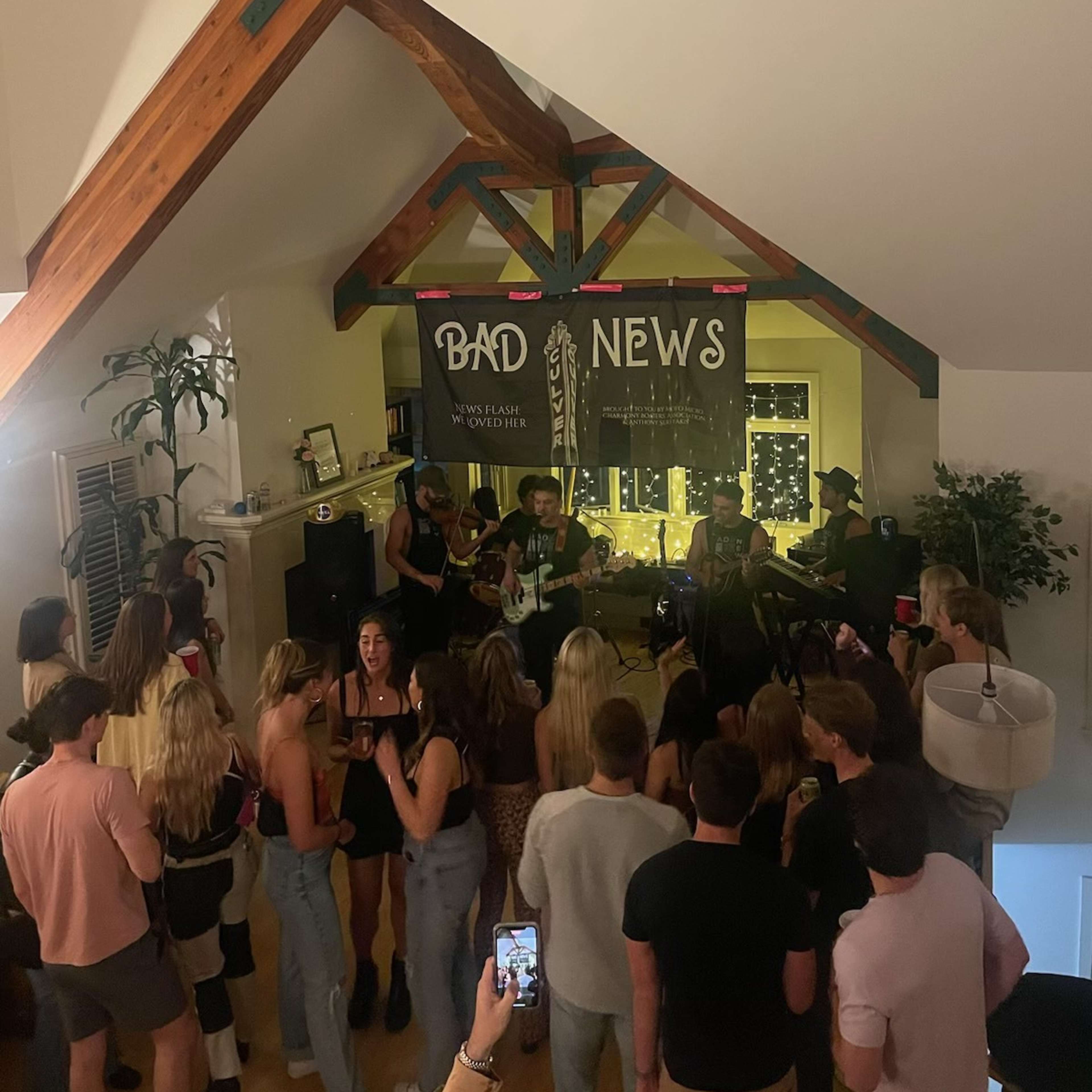 A band performs in a loft space filled with people watching and enjoying the live music.