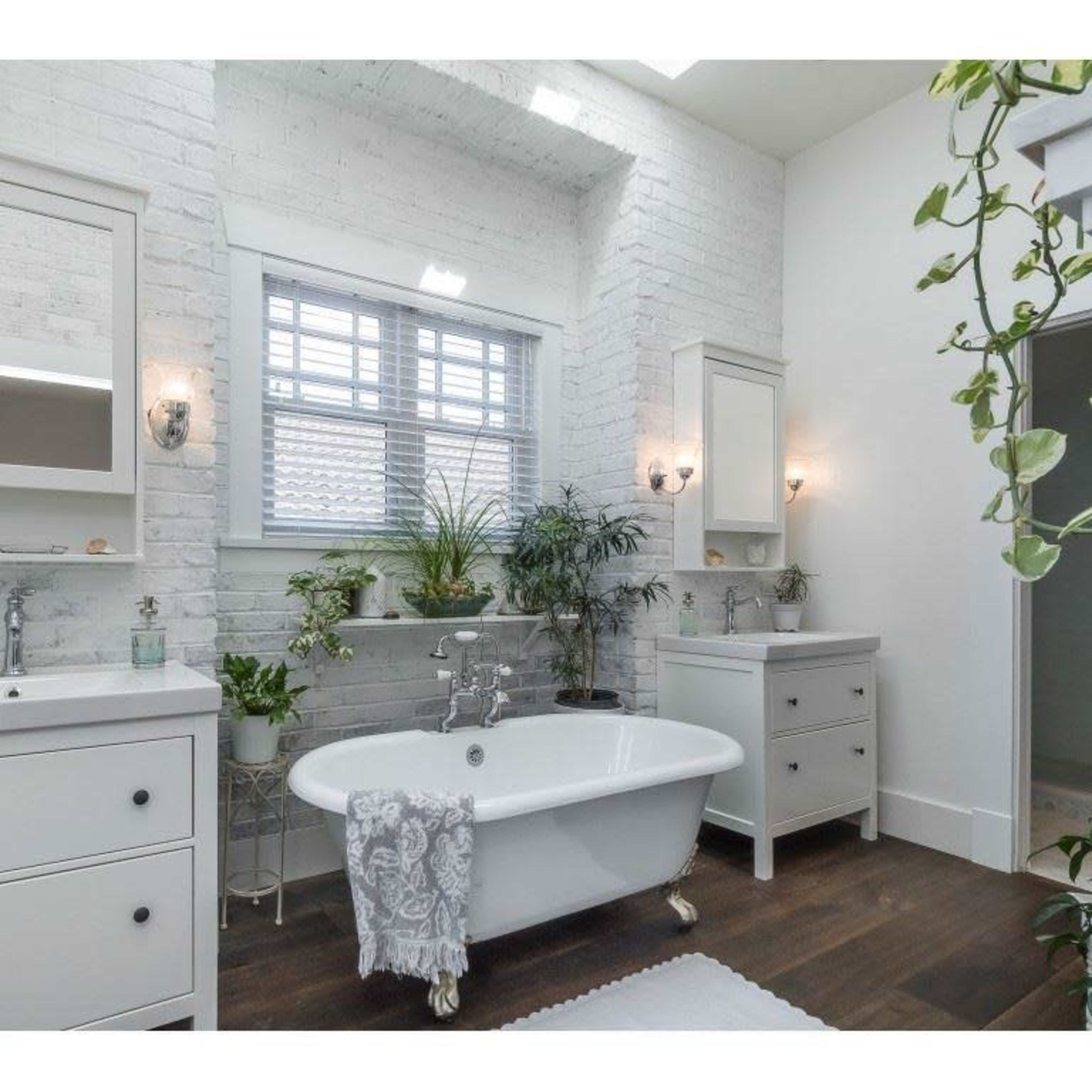 The bathroom features a freestanding bathtub, two sink vanities, and greenery against a white brick wall.