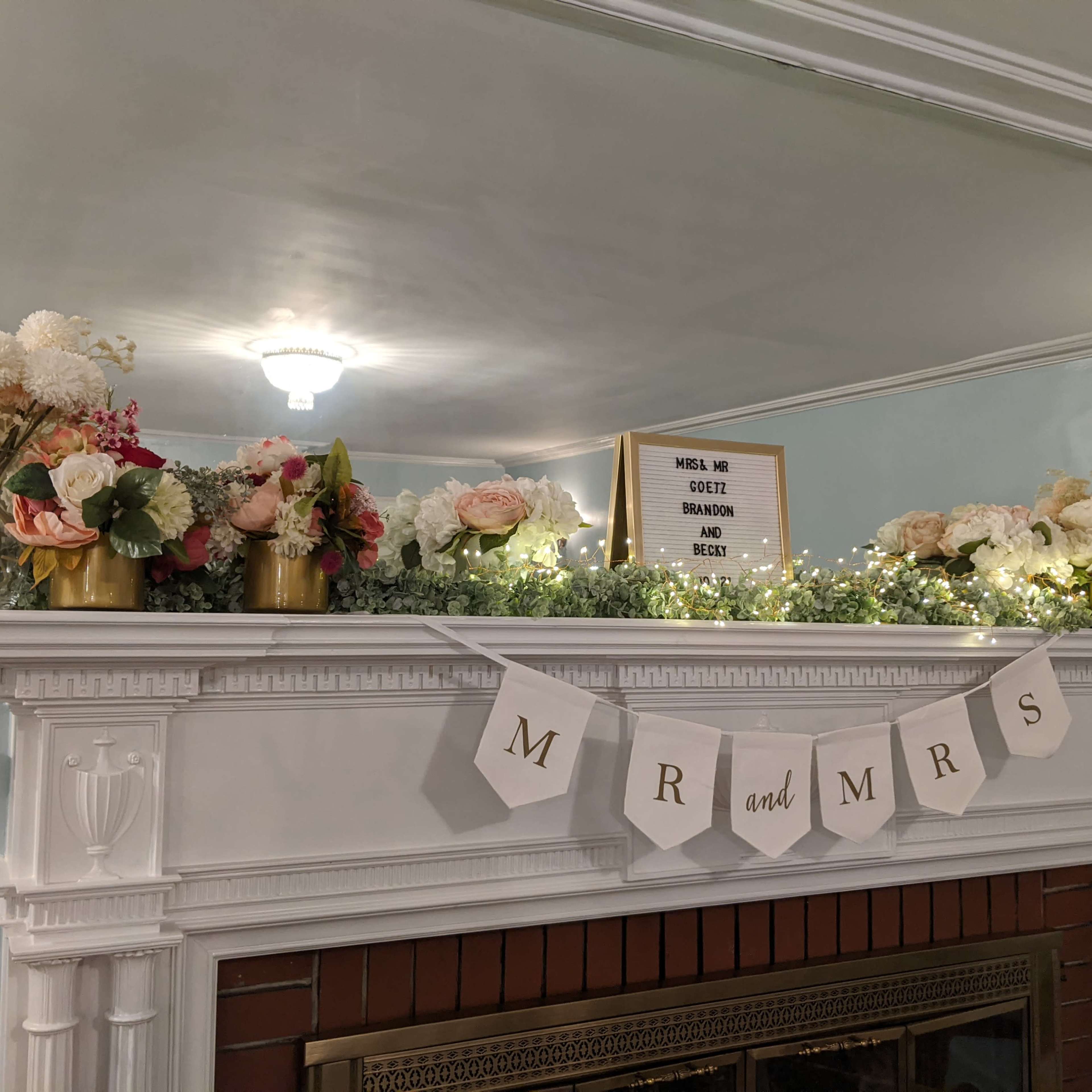 A decorated mantel features a floral arrangement, a sign, and a banner that reads "MR and MRS."