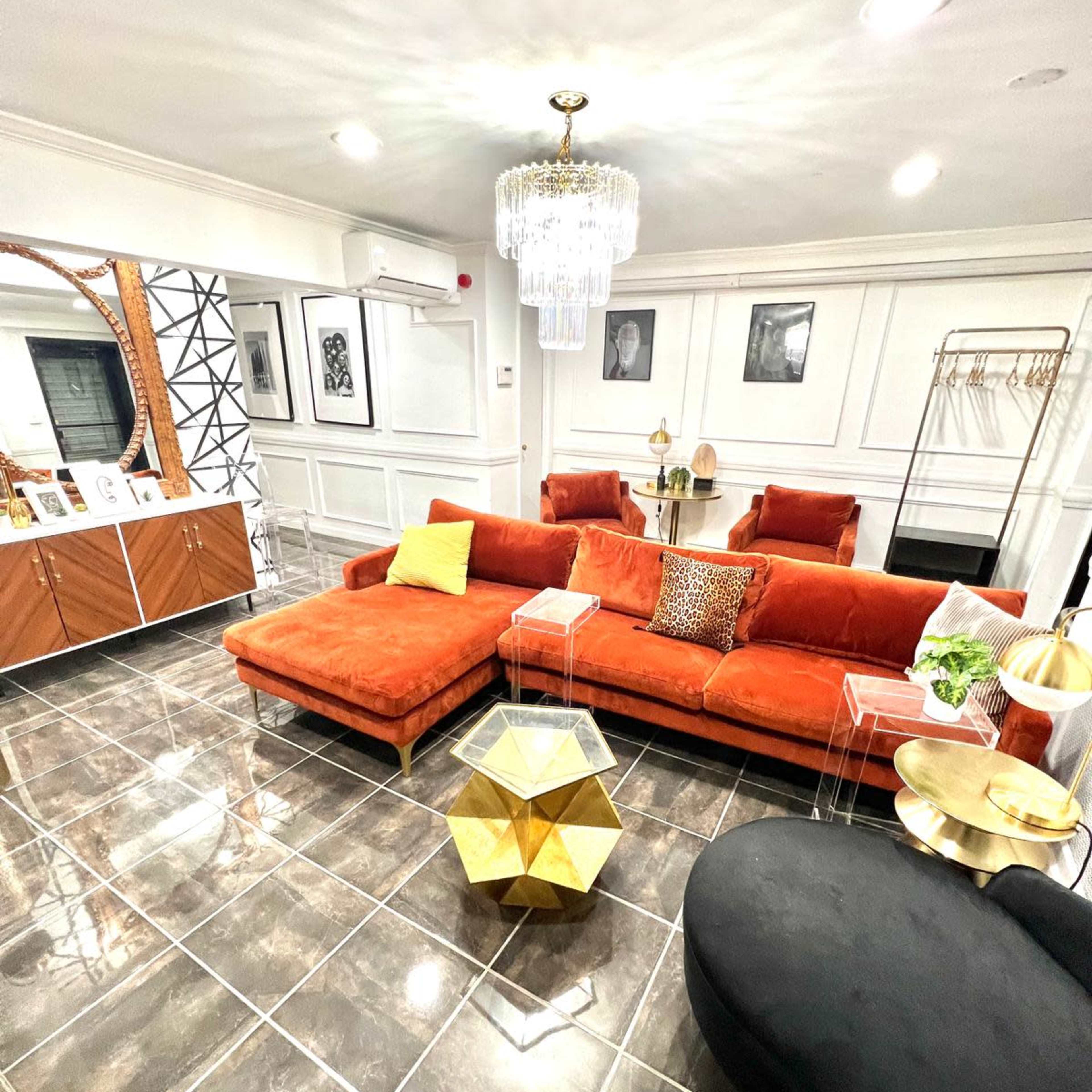 A stylish interior living space featuring an orange sectional sofa, a gold coffee table, and contemporary decor with a chandelier overhead.