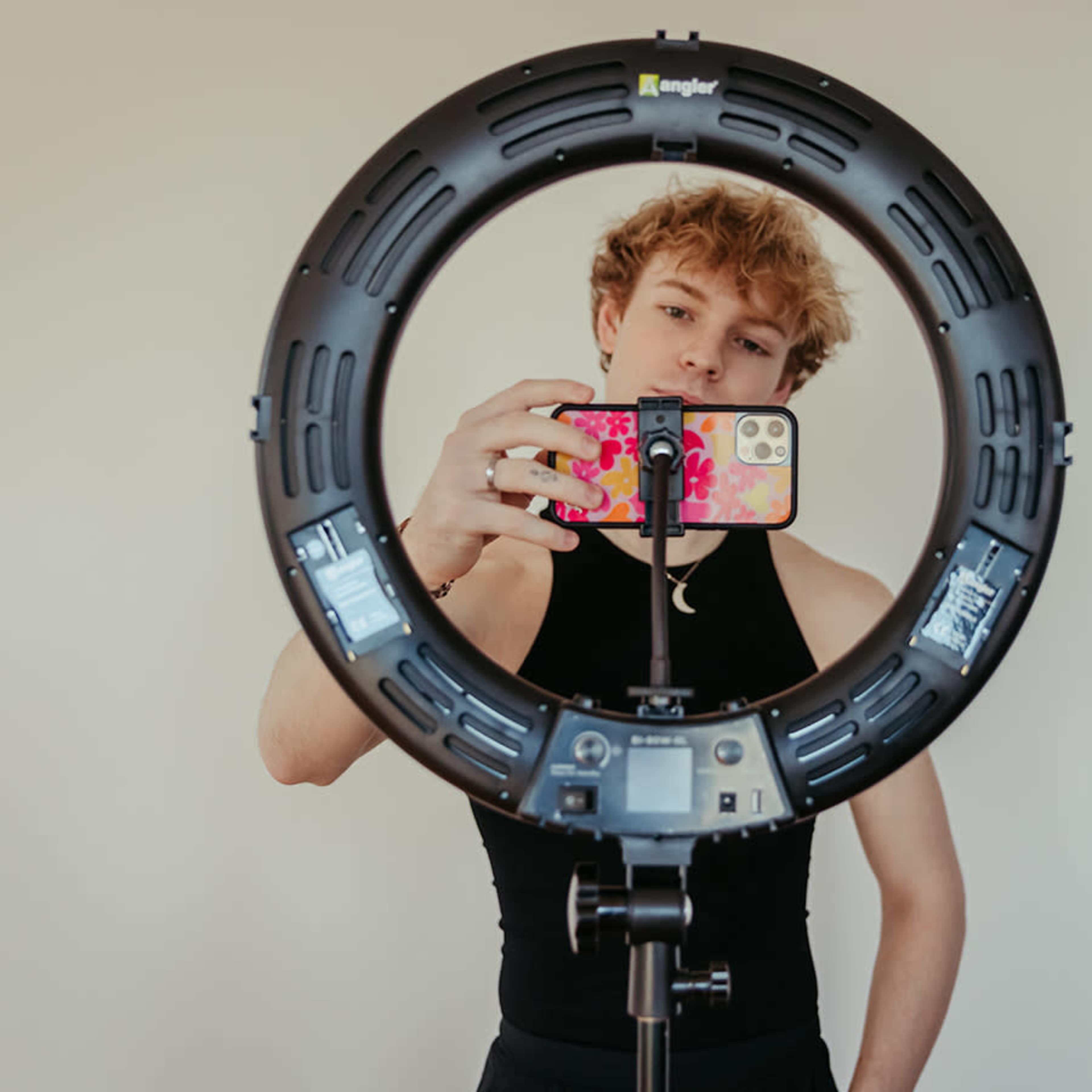 A person is taking a selfie while holding a smartphone in front of a ring light.