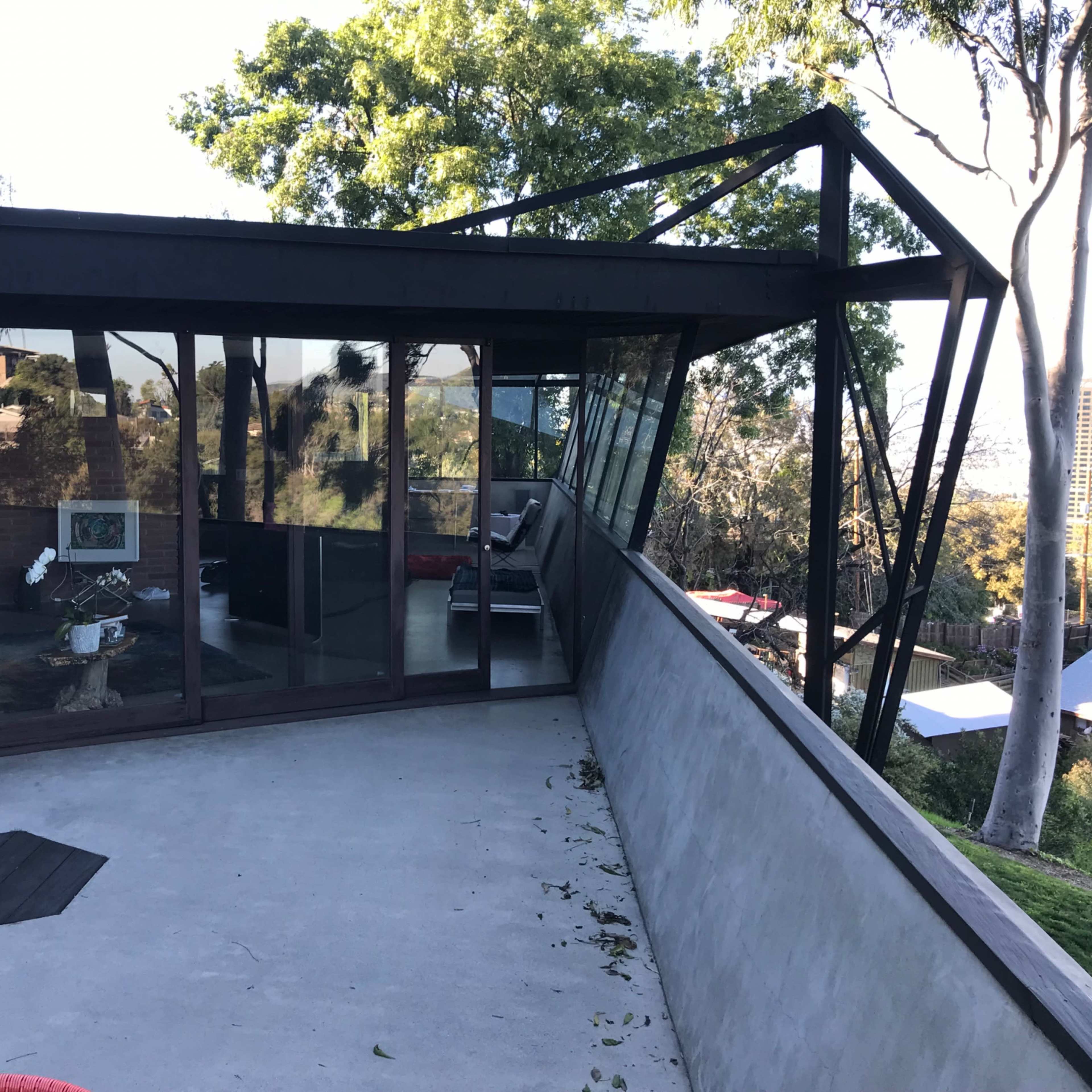 A modern house with a large glass facade and an angular black roof, surrounded by trees.