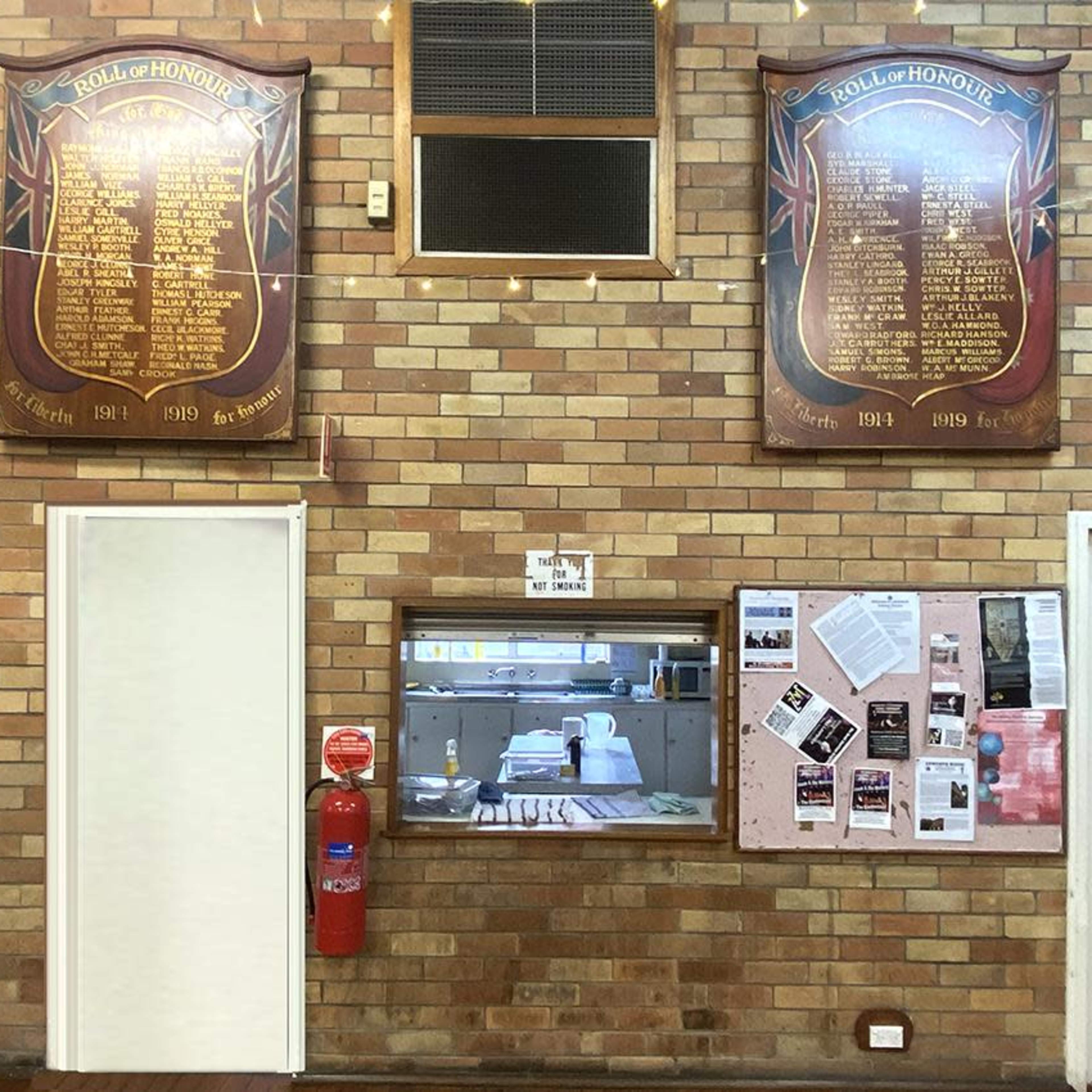 A brick wall with two large honor roll plaques and a serving window, alongside a bulletin board with various papers attached.