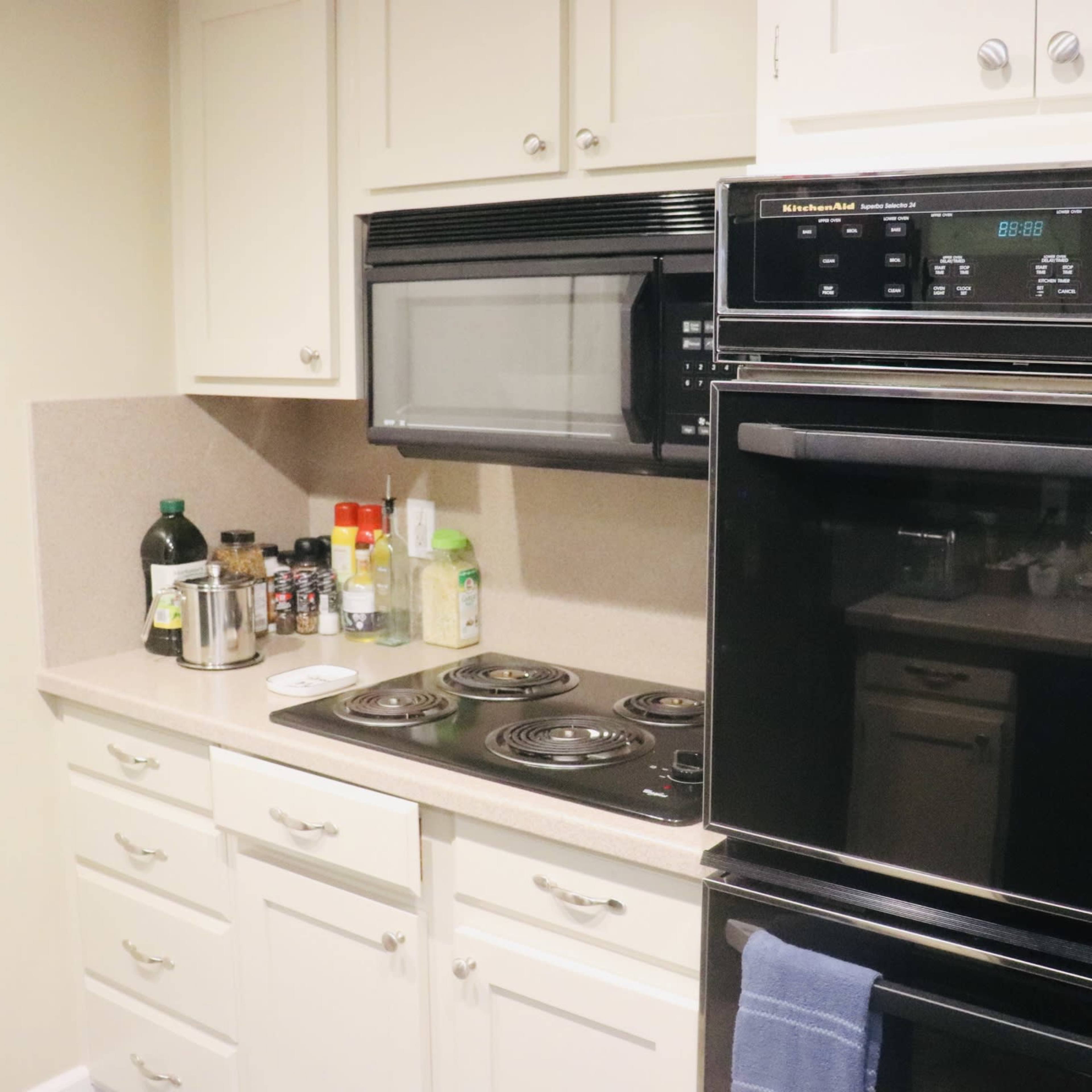 A kitchen with a countertop, a microwave above an oven, and various bottles and utensils on the surfaces.