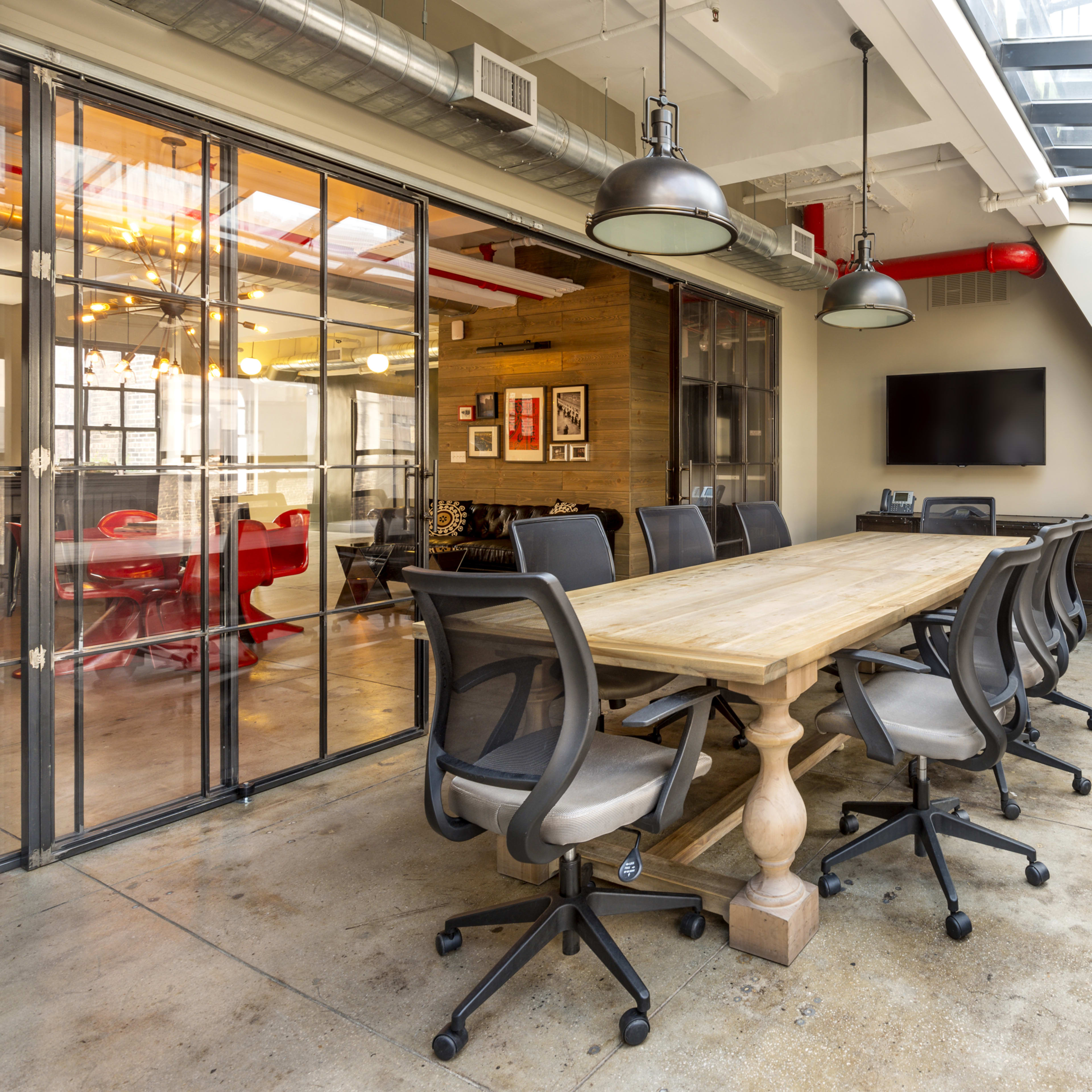 A conference room features a large wooden table surrounded by ergonomic chairs, with glass walls and ample natural light.