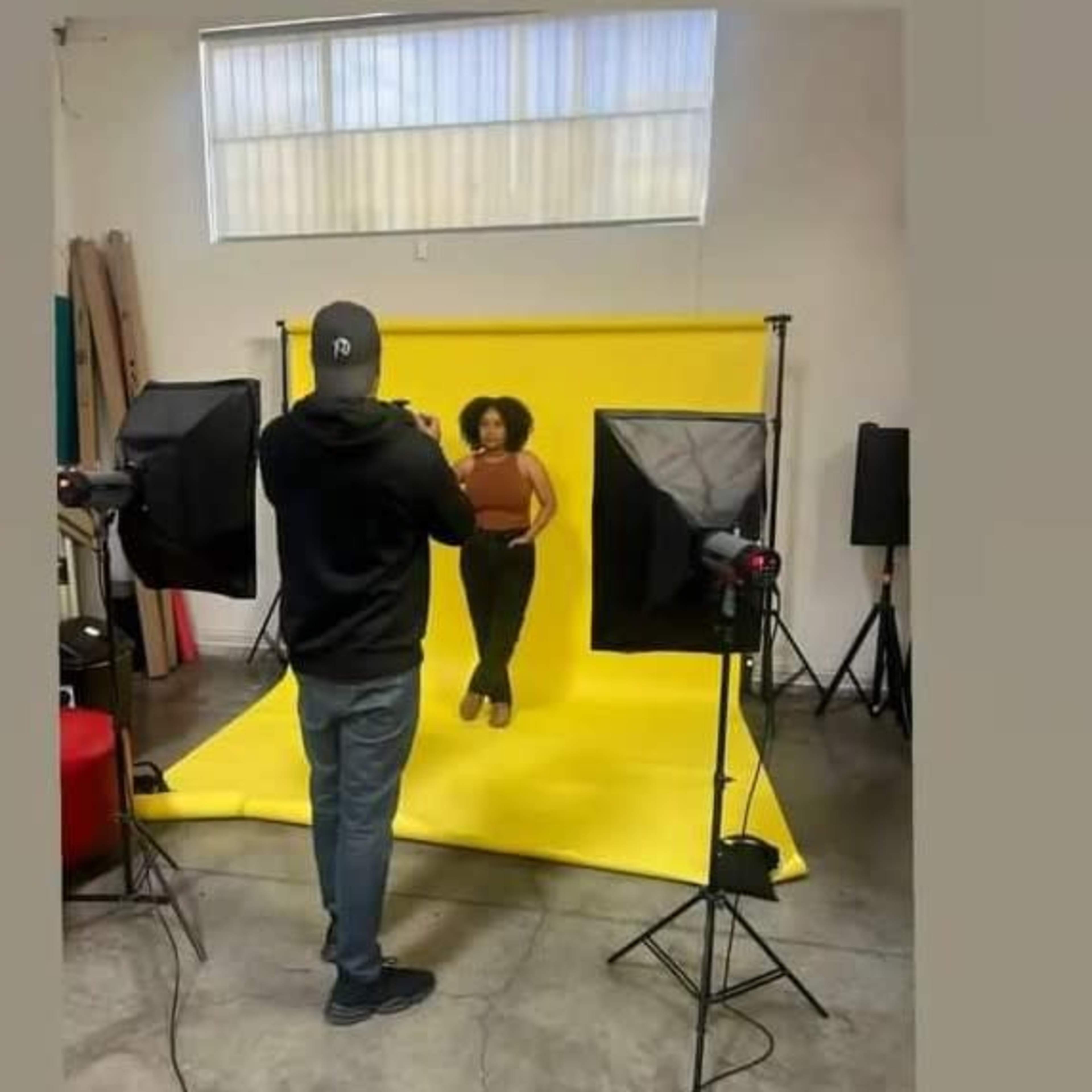 A photographer captures a model posing against a bright yellow backdrop in a studio setting.
