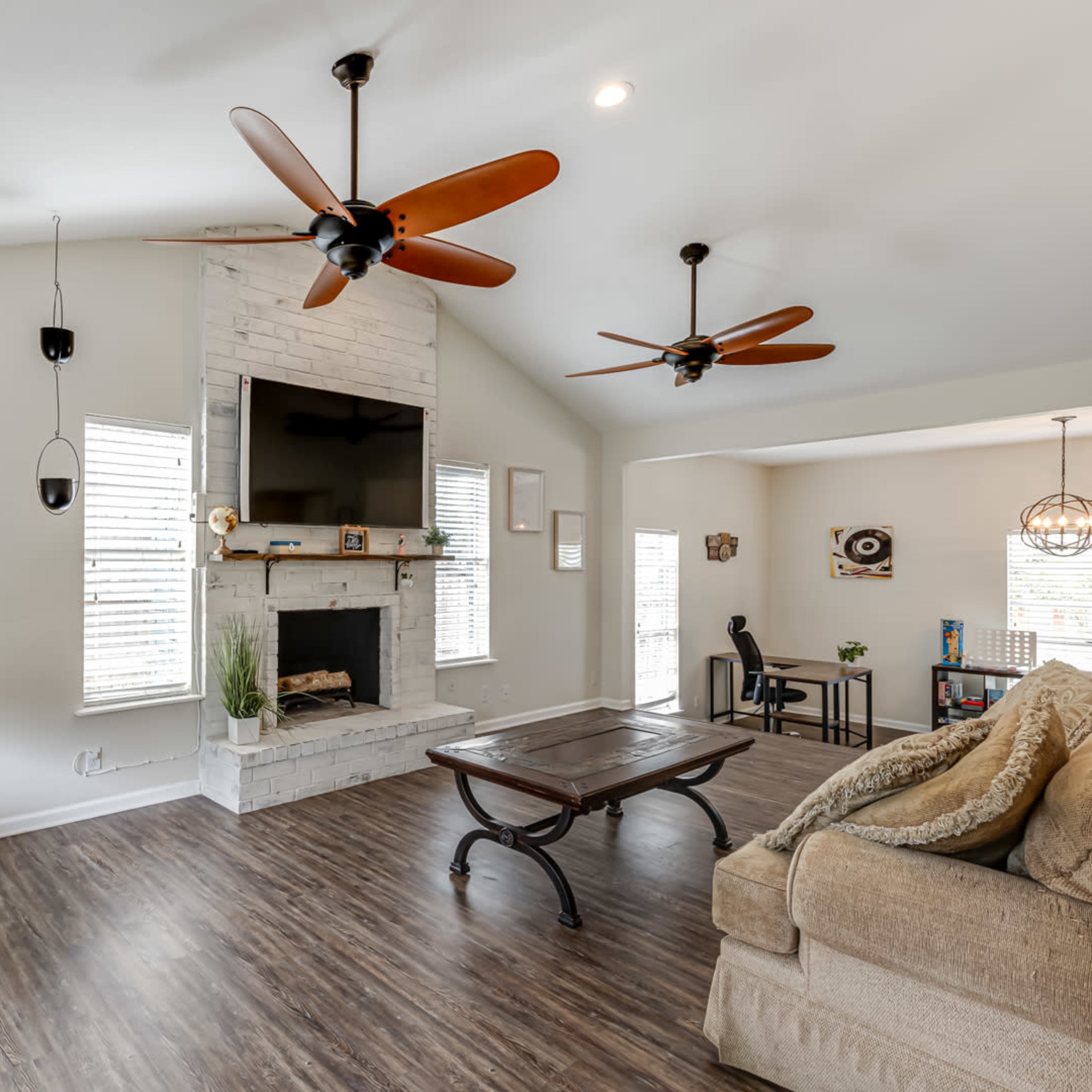 A modern living room with two ceiling fans, a stone fireplace, and a large television above it, featuring a sectional sofa and a coffee table.