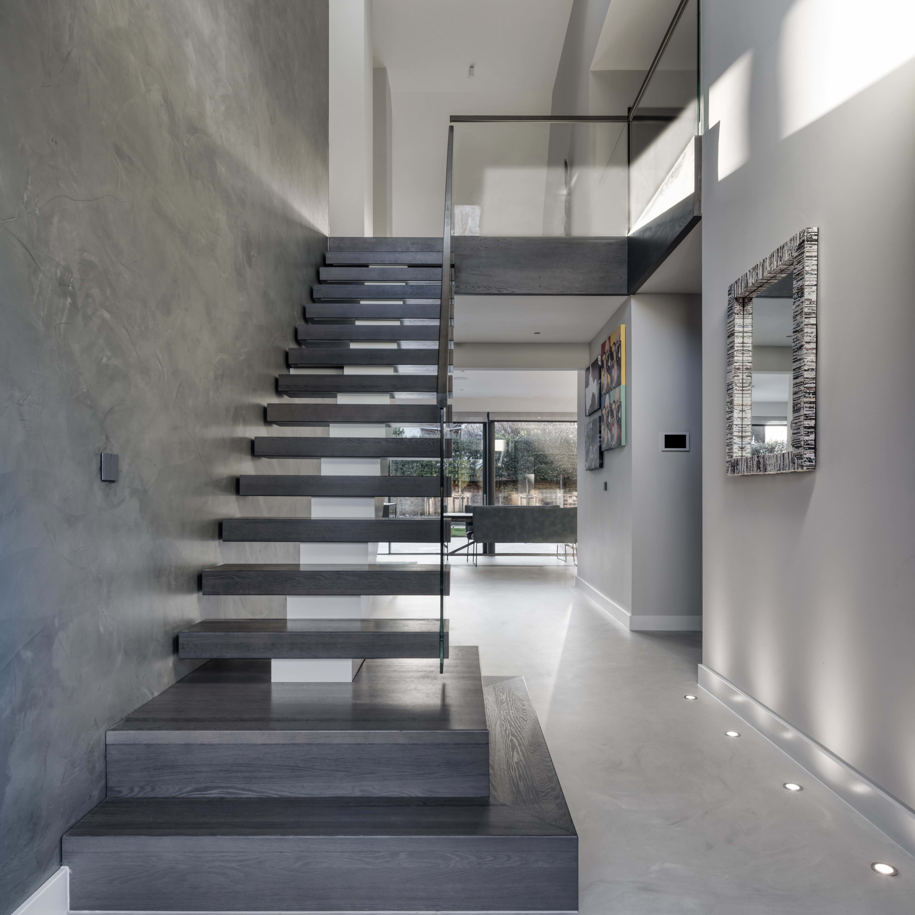 A modern staircase with open treads and a glass railing ascends in a well-lit hallway.