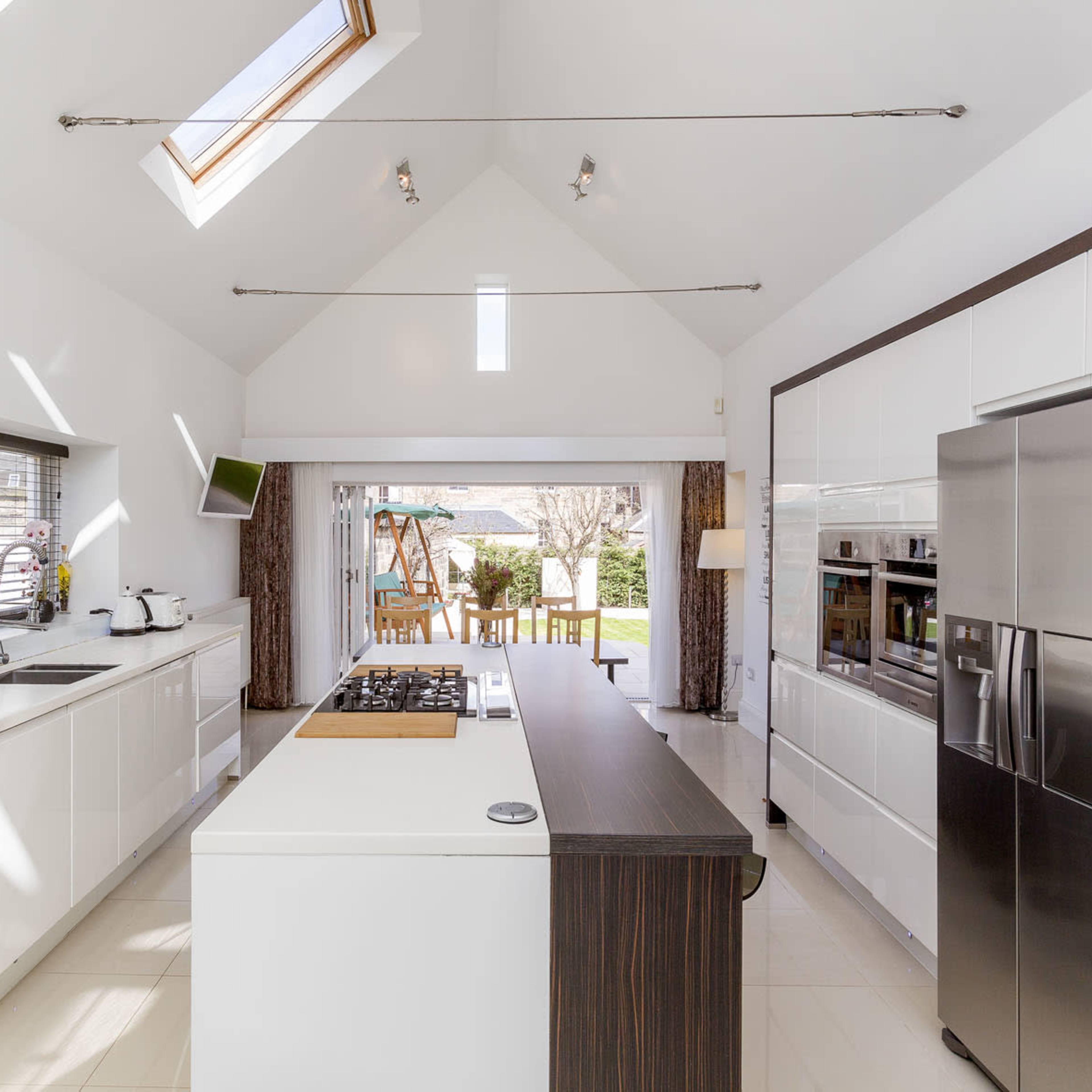 A modern kitchen featuring white cabinetry, a central island with a cooktop, and large windows leading to an outdoor dining area.