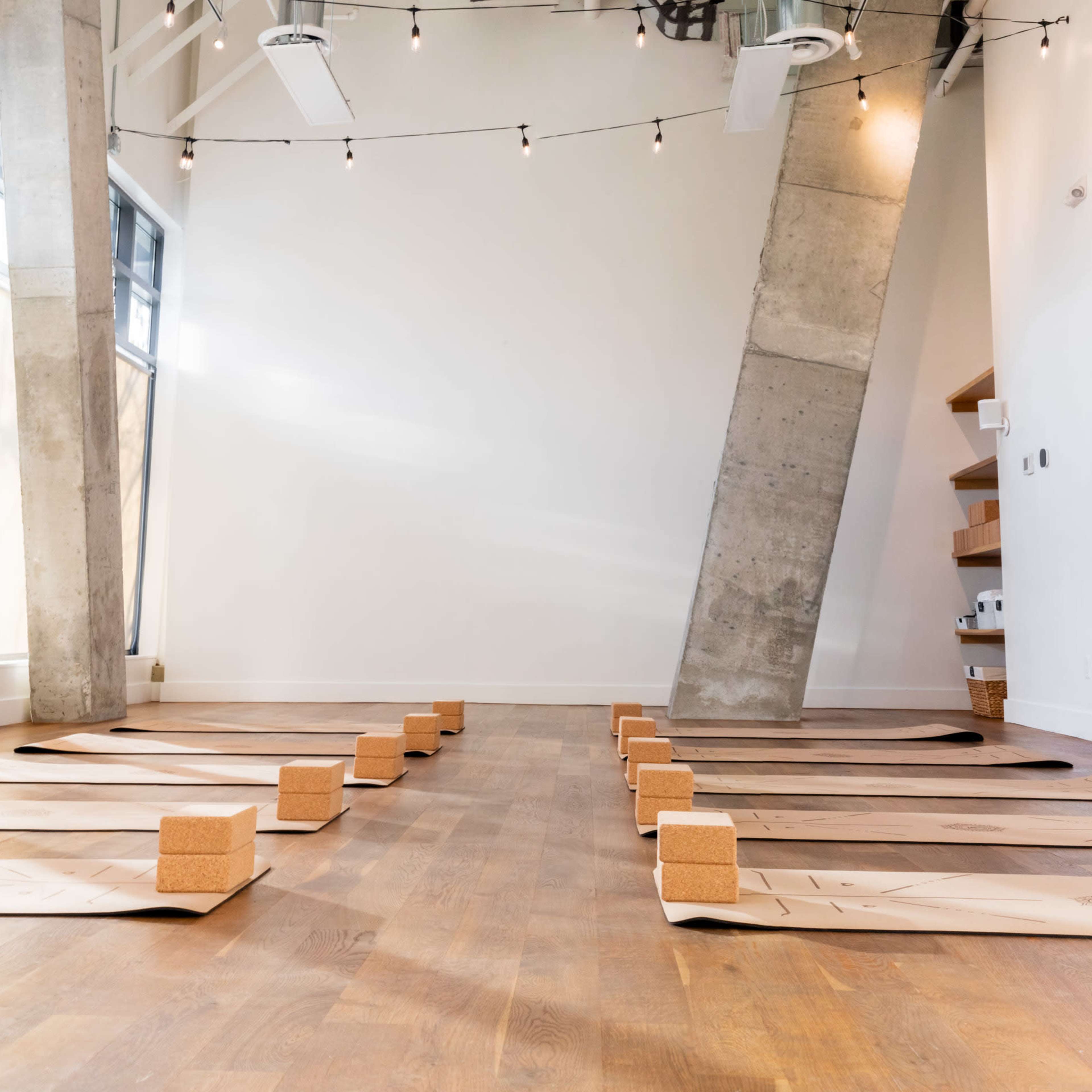 A yoga studio features wooden flooring with neatly arranged mats and cork blocks under soft lighting.
