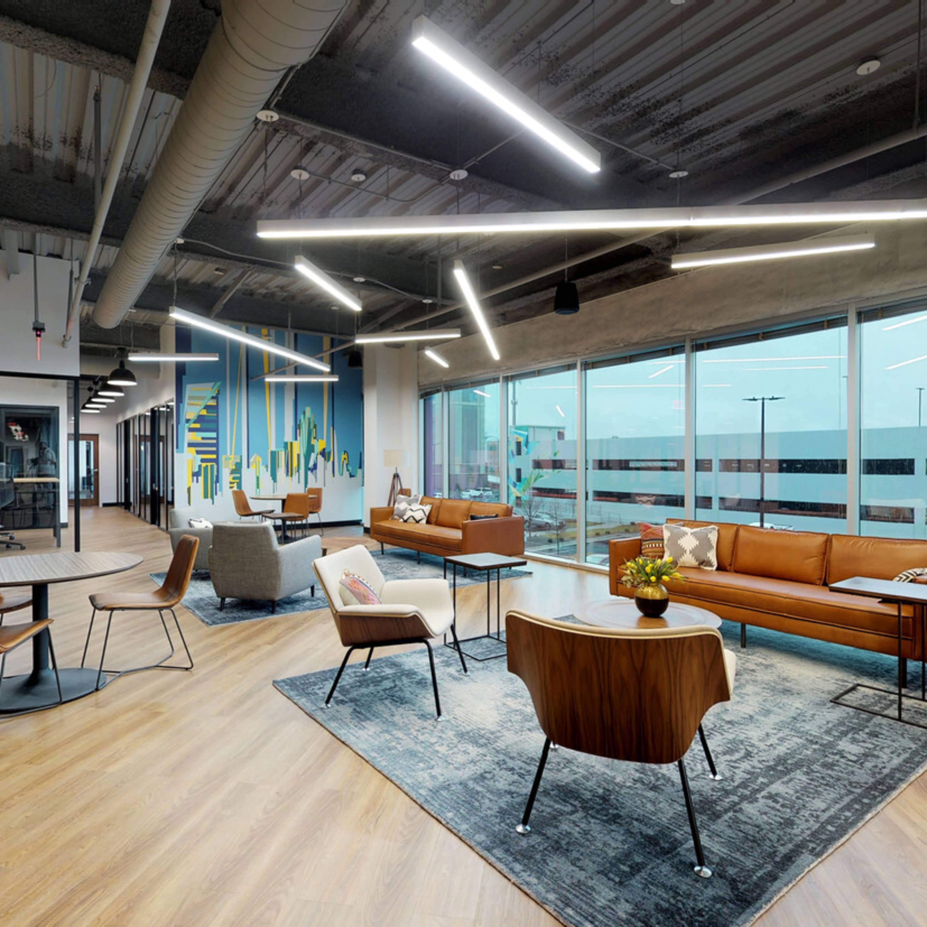 A modern office lounge area with a brown leather sofa, stylish chairs, and large windows providing natural light.