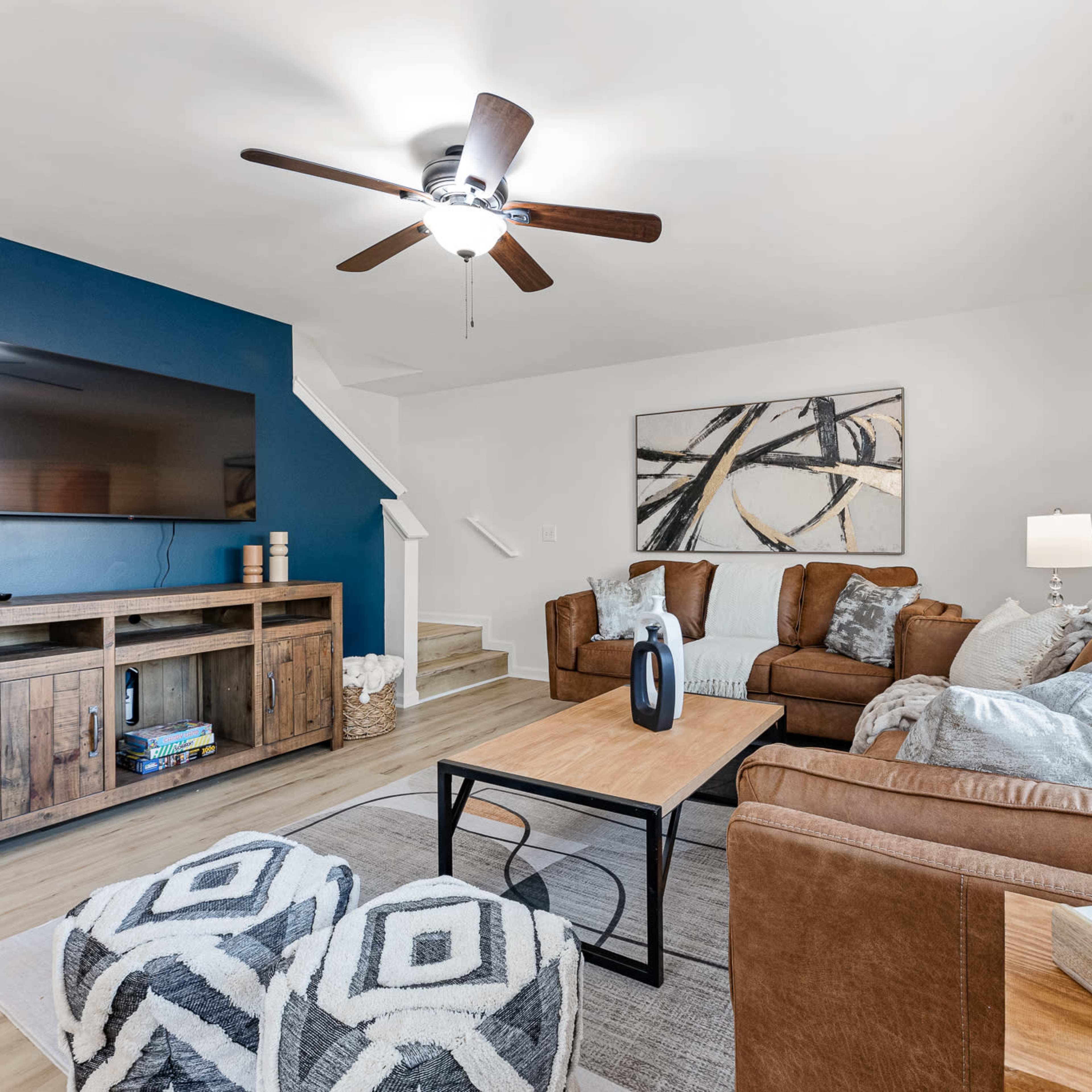 The living room features a brown sofa set, a wooden media console with a flat-screen TV, and a coffee table, with a blue accent wall in the background.