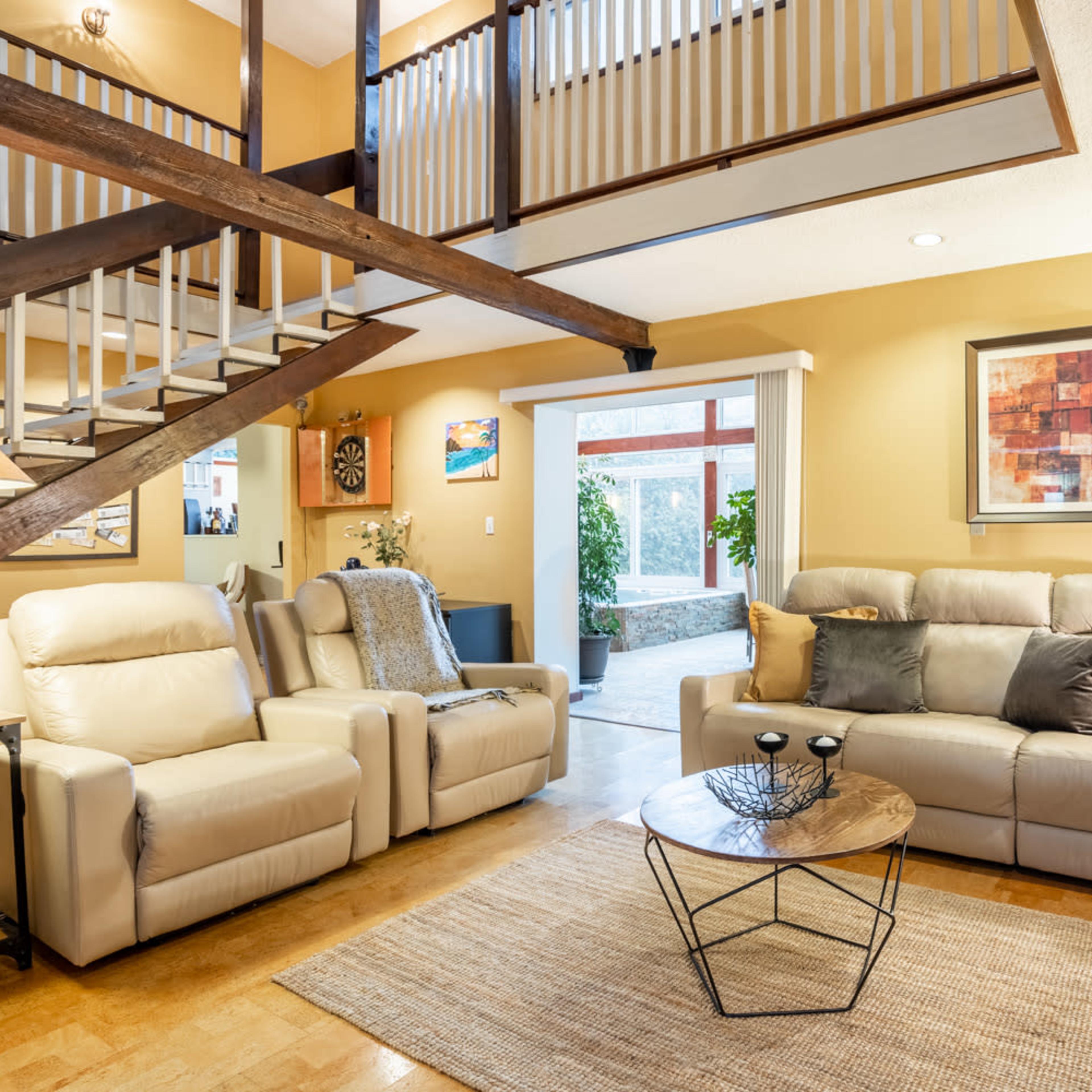 A cozy living room with beige leather sofas, a glass coffee table, and a staircase leading to an upper level.