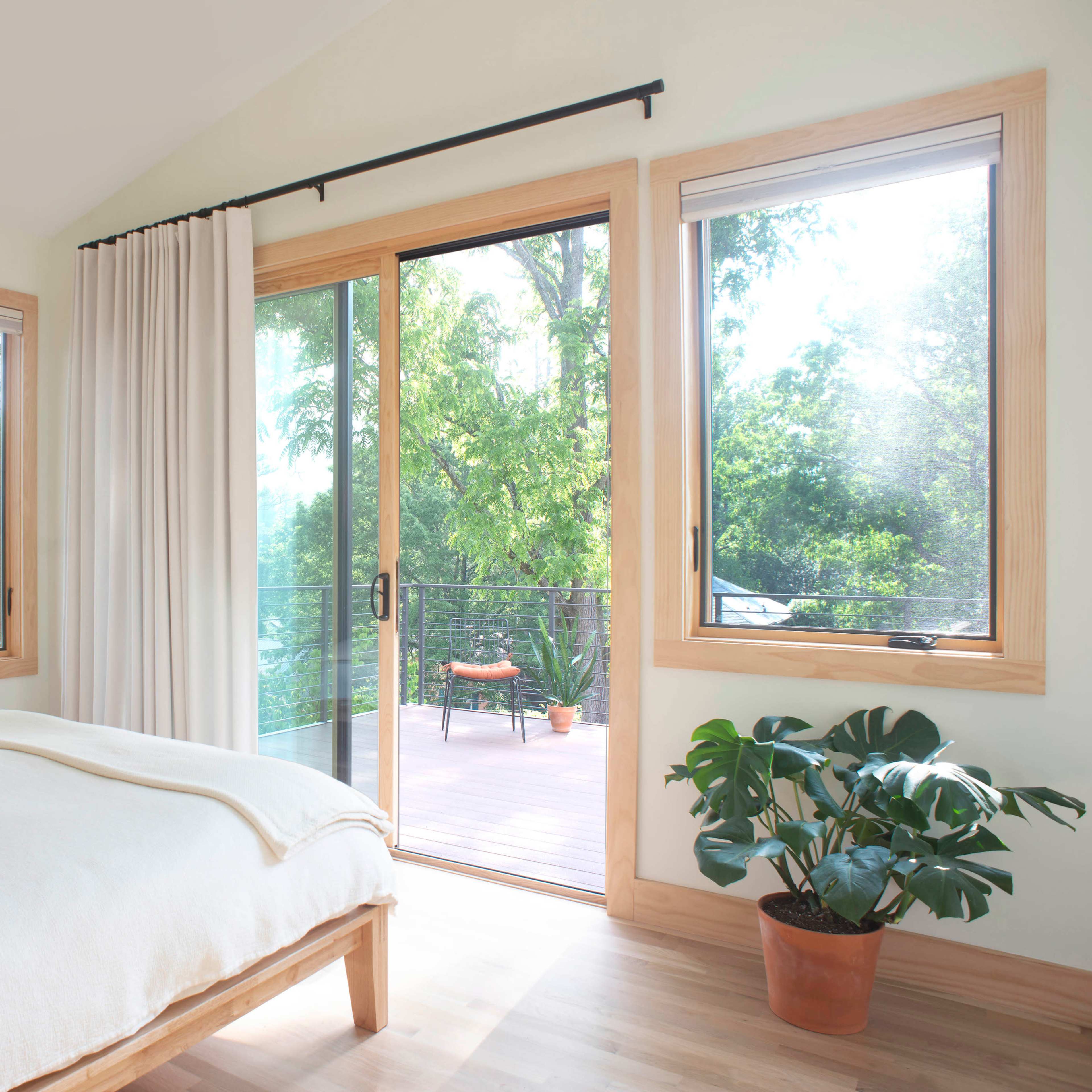 A bright bedroom features a bed positioned beside large windows that open to a deck with outdoor seating.