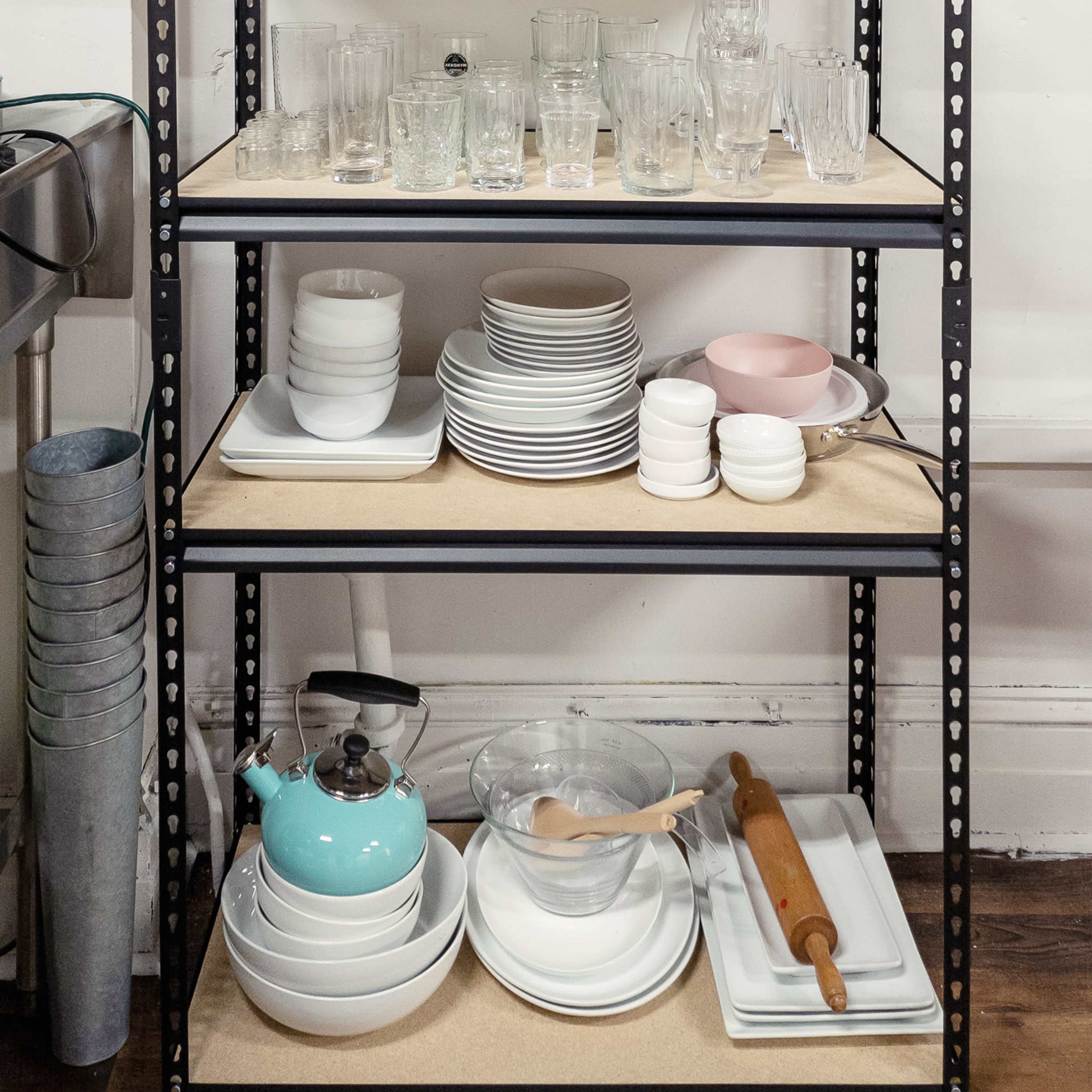 A metal shelving unit displays various glassware, dishes, and kitchen utensils arranged in four rows.