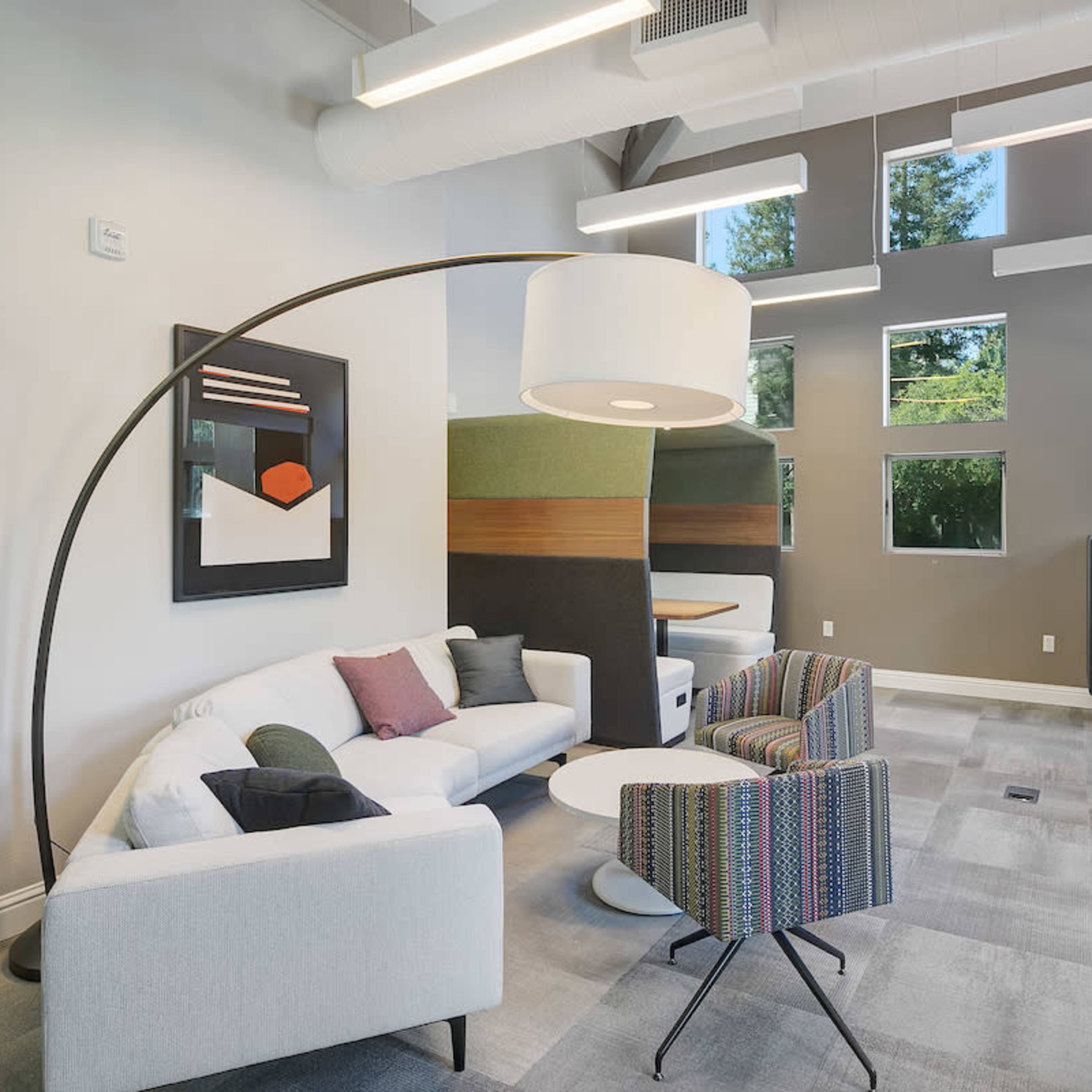 A modern lounge area with a curved floor lamp, a white sofa, a colorful armchair, and large windows allowing natural light.