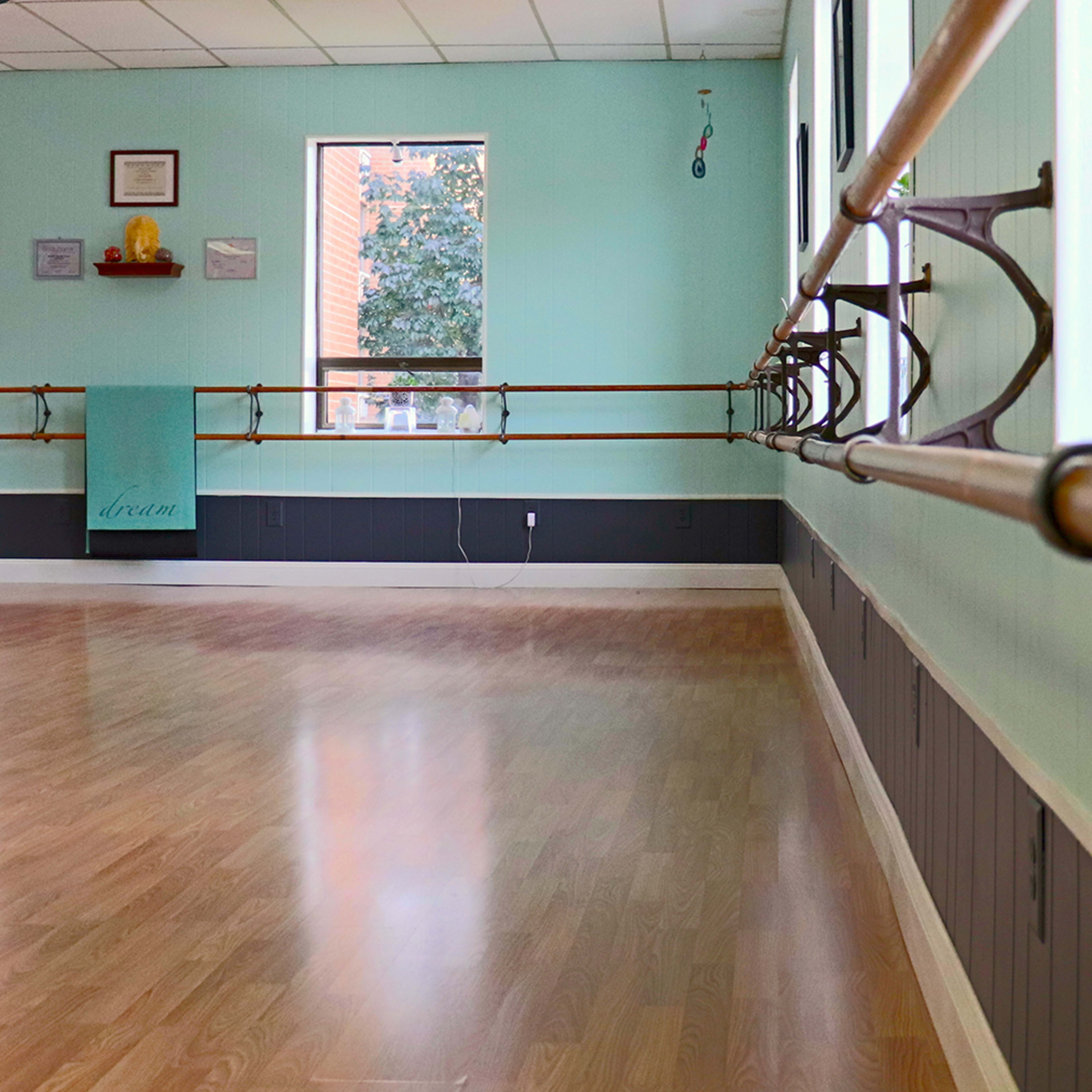 A dance studio with wooden ballet bars, light-colored walls, and large windows allowing natural light to enter.