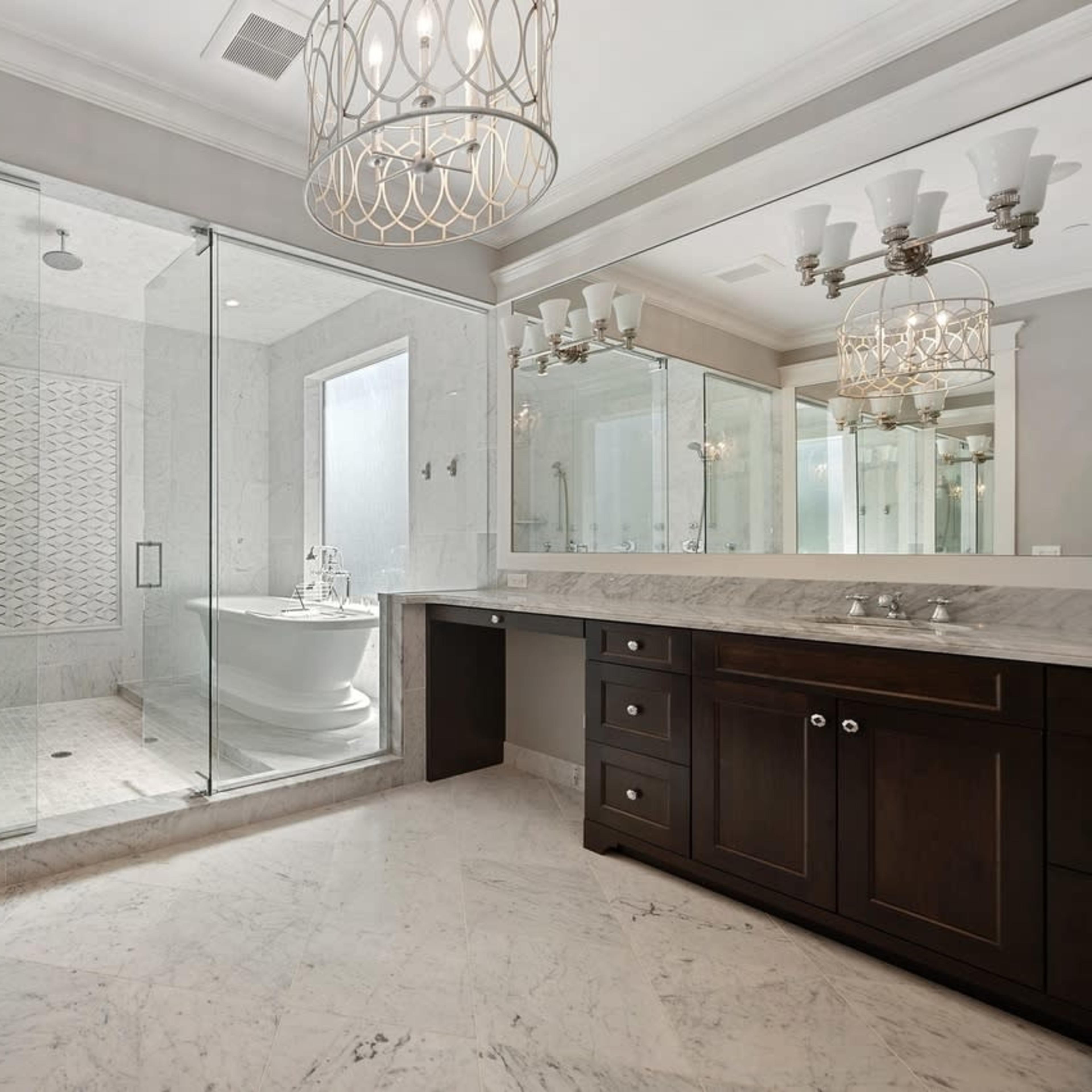 A modern bathroom featuring a glass-enclosed shower, a freestanding bathtub, dual vanities with dark wood cabinetry, and marble flooring.