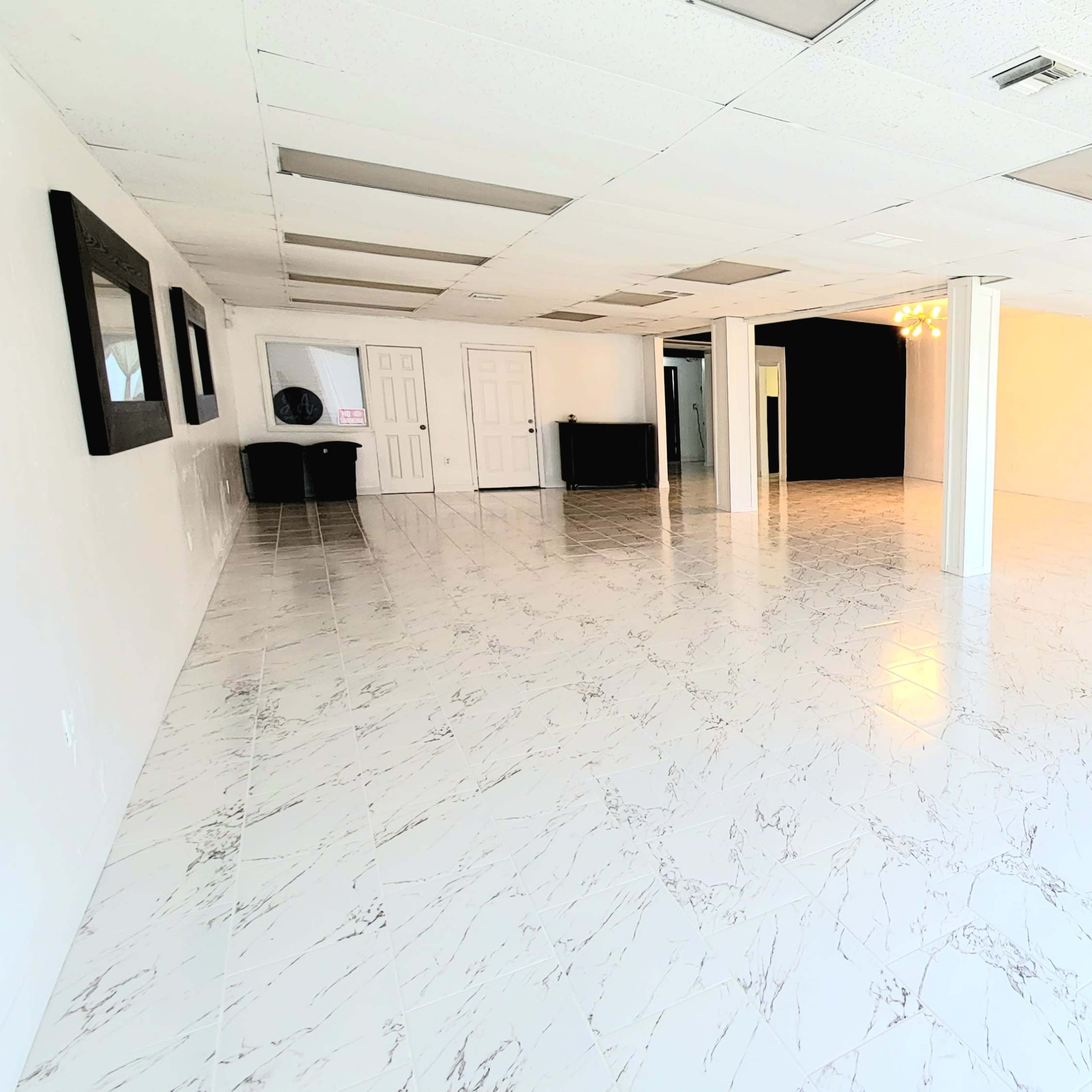 A spacious empty room with marble-patterned tile flooring, white walls, and several ceiling lights.