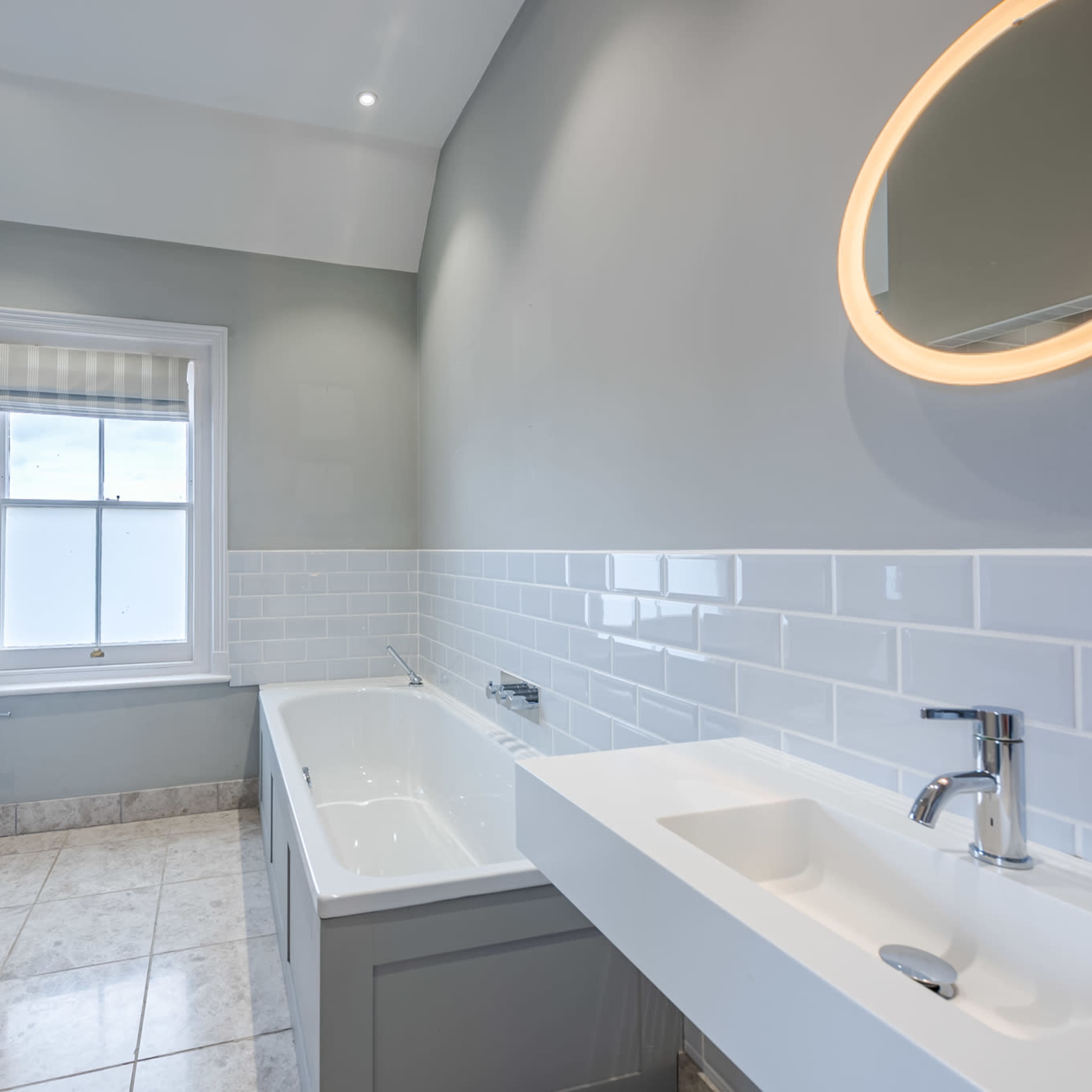 A modern bathroom featuring a bathtub, a sink with a faucet, and large wall tiles in a light gray color.