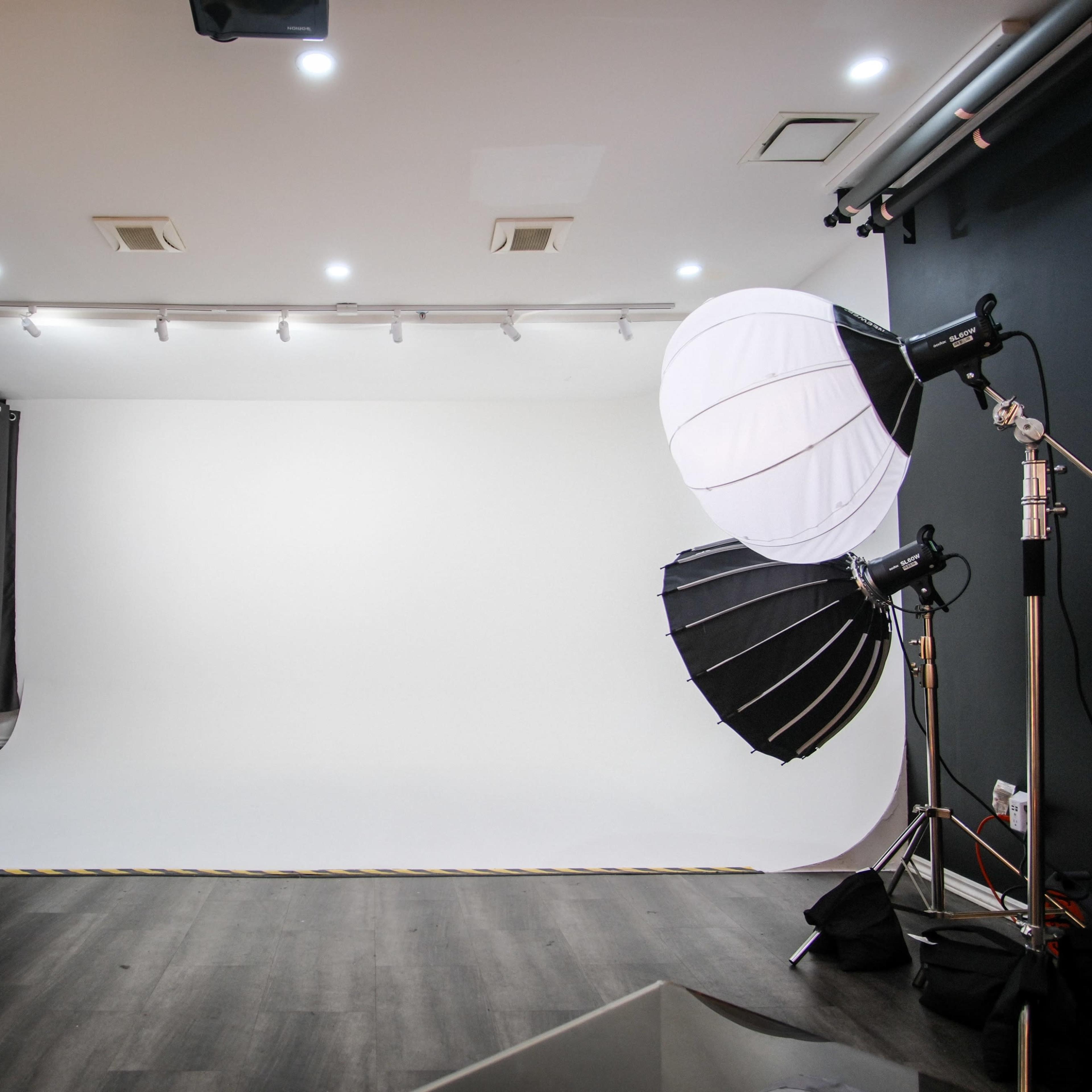 A photography studio with a white backdrop, lighting equipment, and dark curtains.