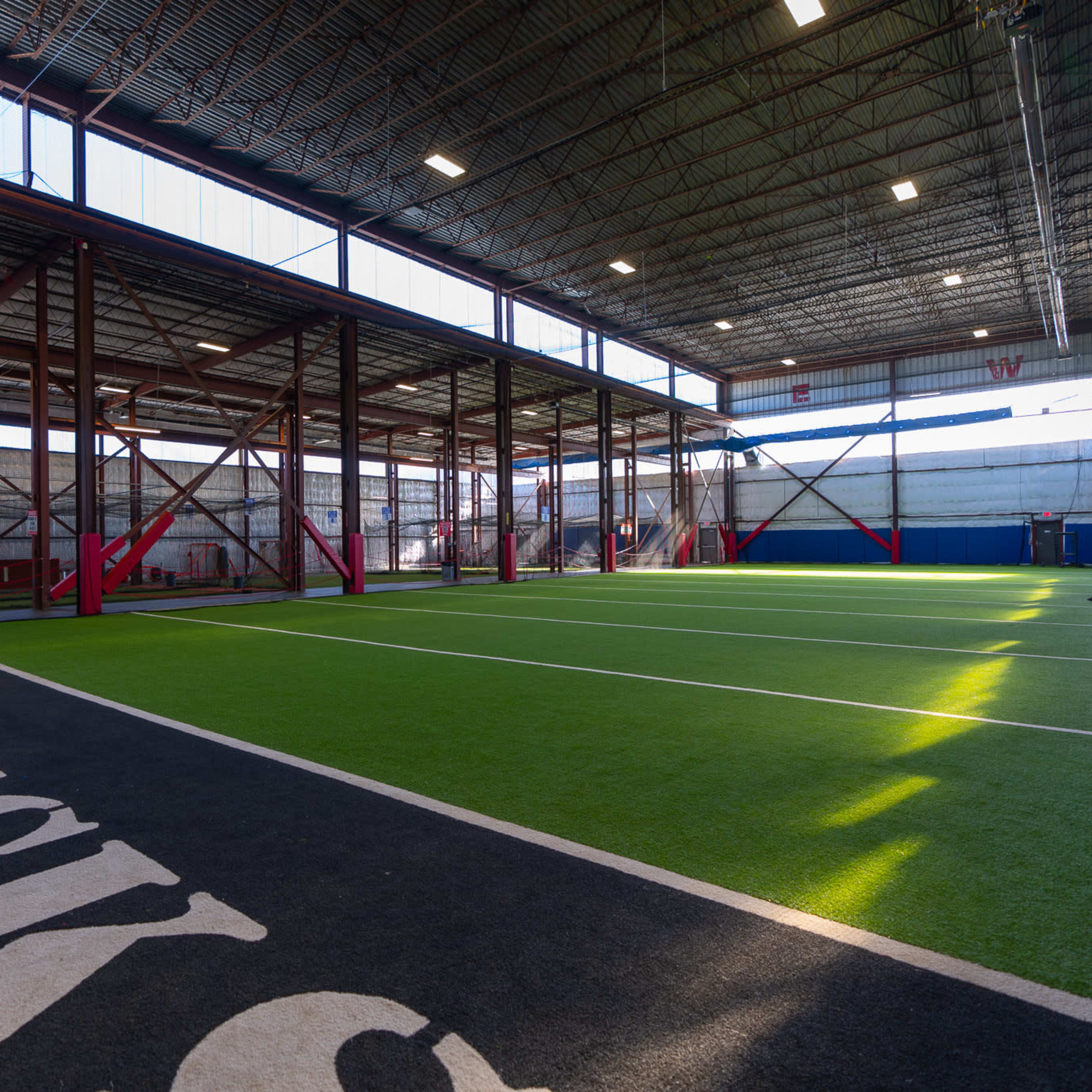 A spacious indoor sports facility with artificial turf and designated training areas.