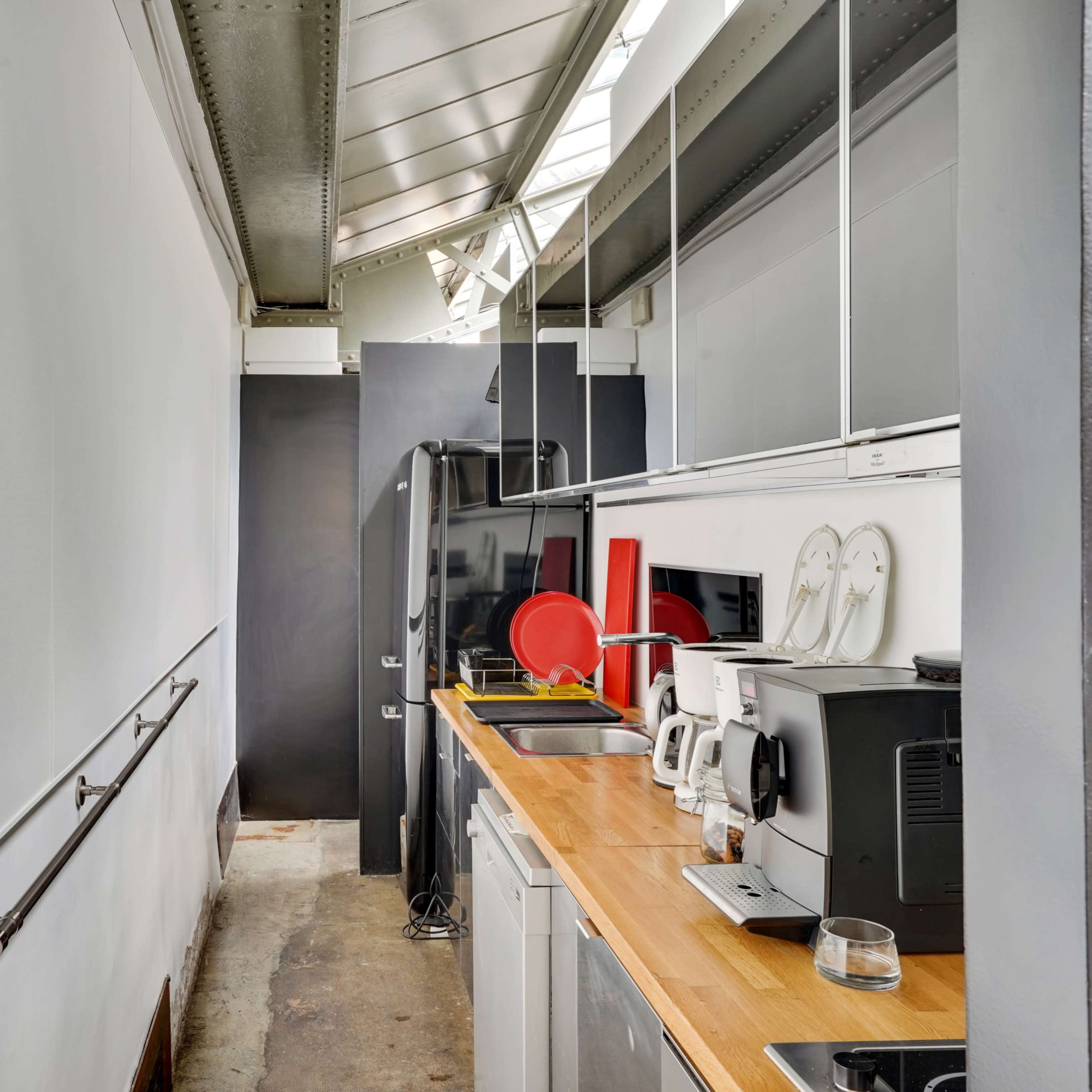 A narrow kitchen corridor with a wooden countertop, appliances, and a wall-mounted intercom system.