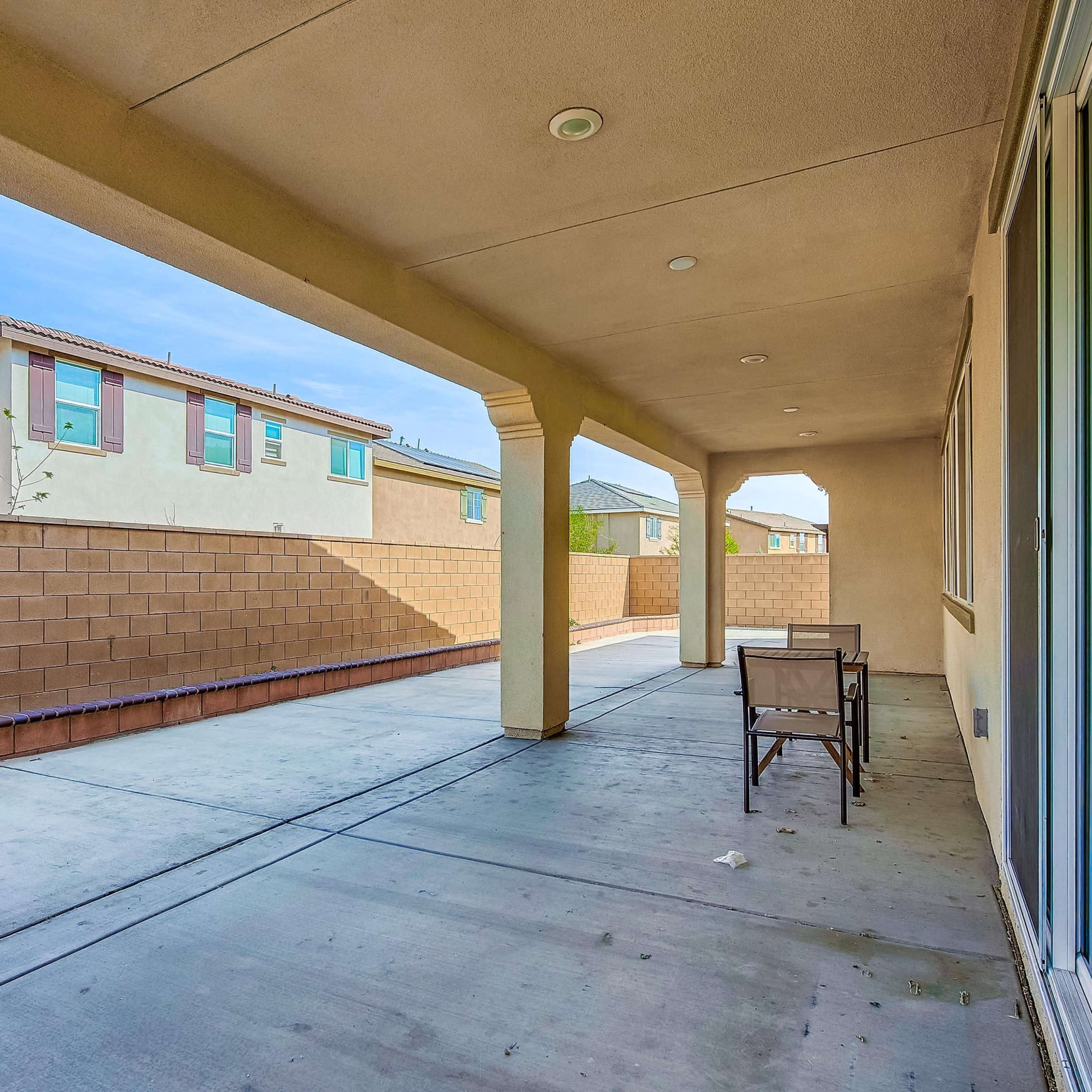 A covered patio area adjacent to a wall with neighboring houses visible in the background.