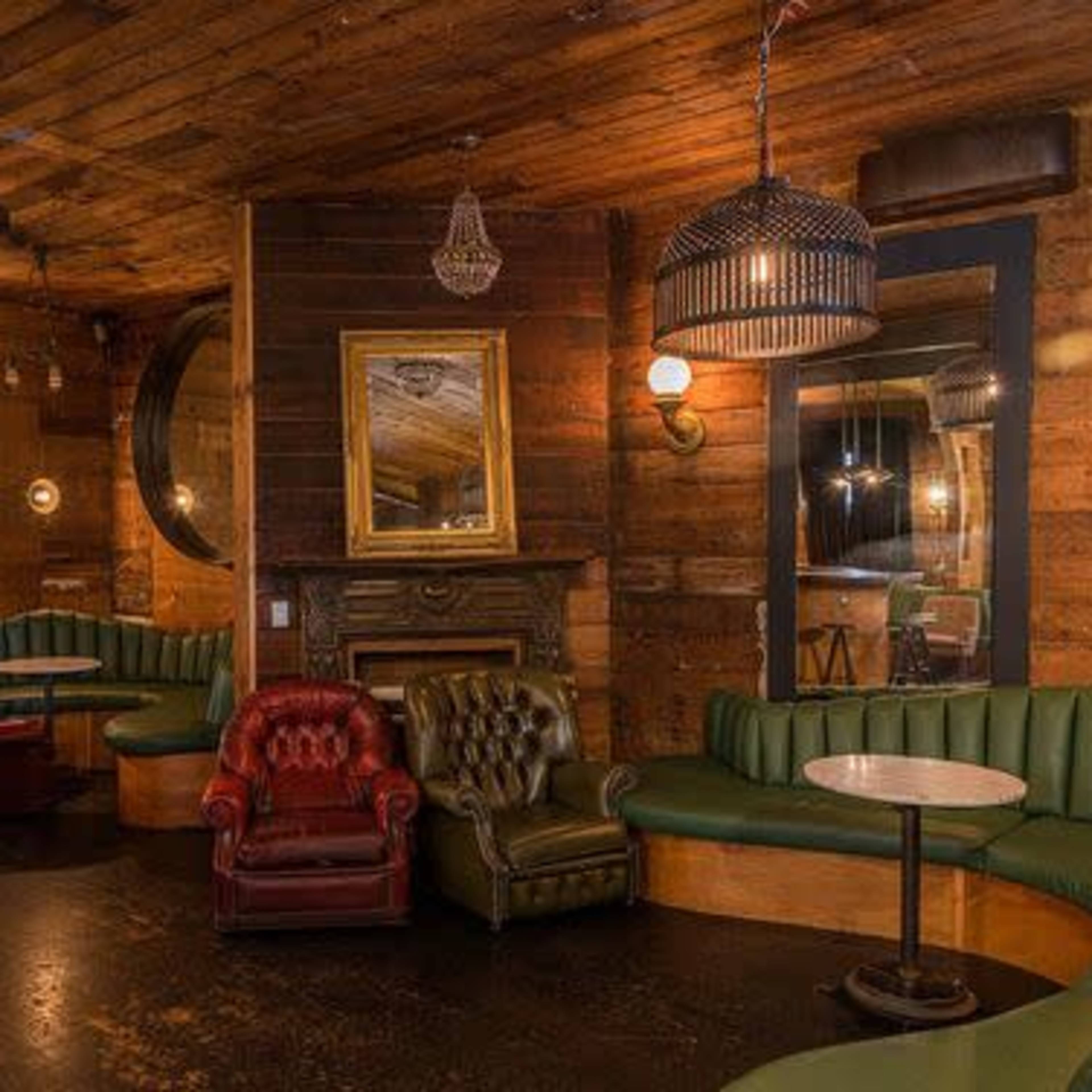 A cozy bar interior with wooden walls, plush green seating, and a mix of ambient lighting fixtures.