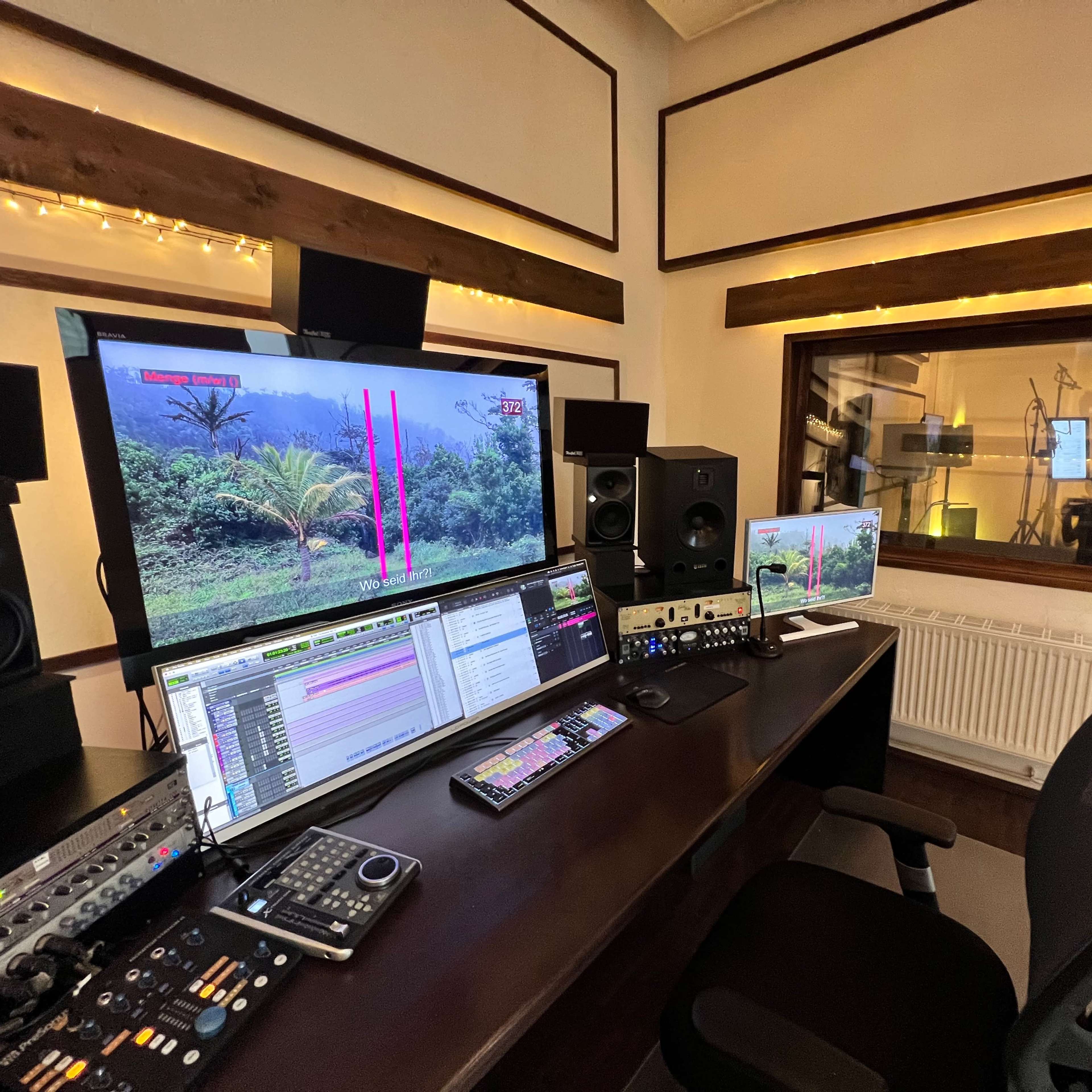 A modern audio production studio features multiple monitors displaying a lush landscape while equipped with various sound mixing and recording equipment.