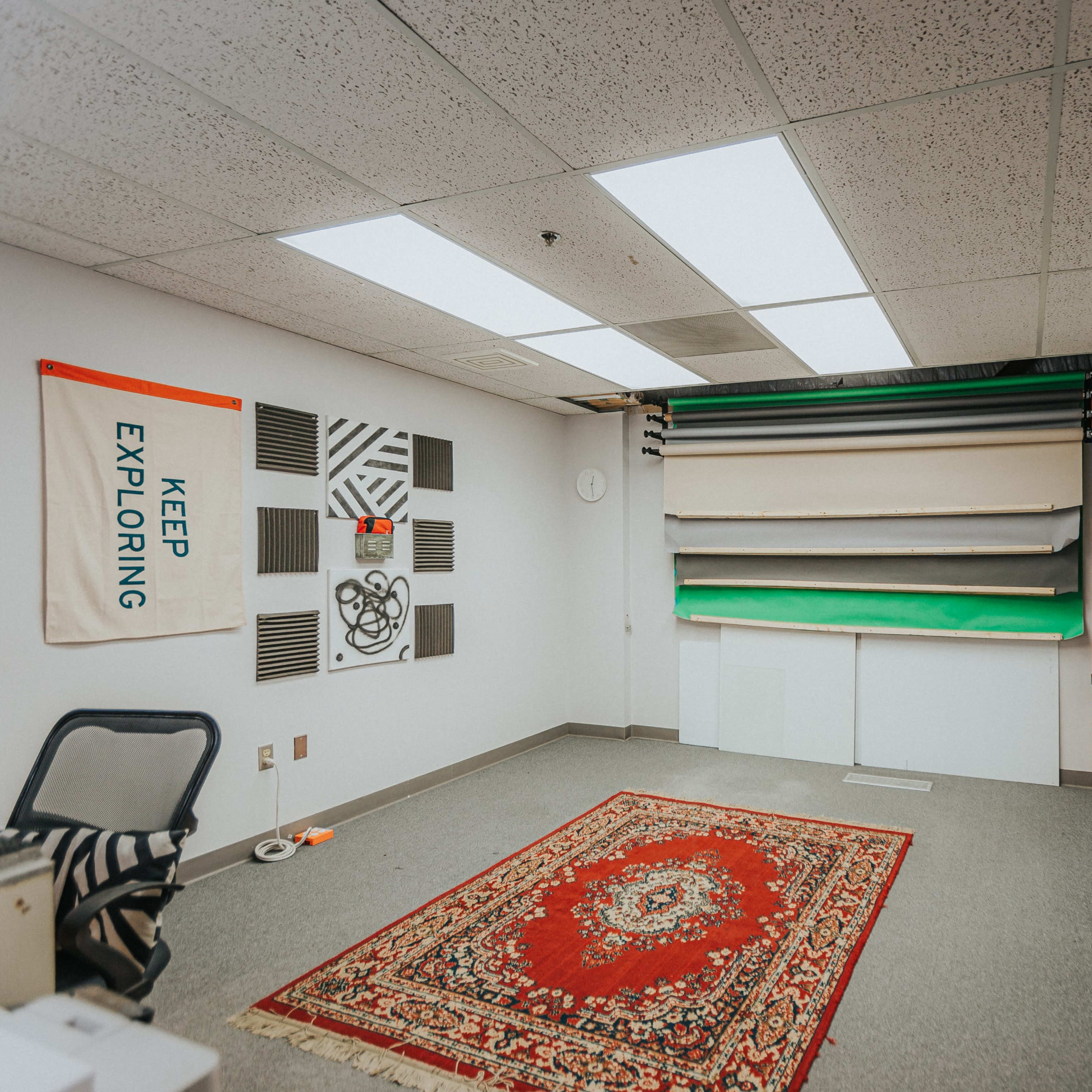 A spacious studio room with a patterned area rug, large mirrors, and a backdrop setup consisting of colored rolls.