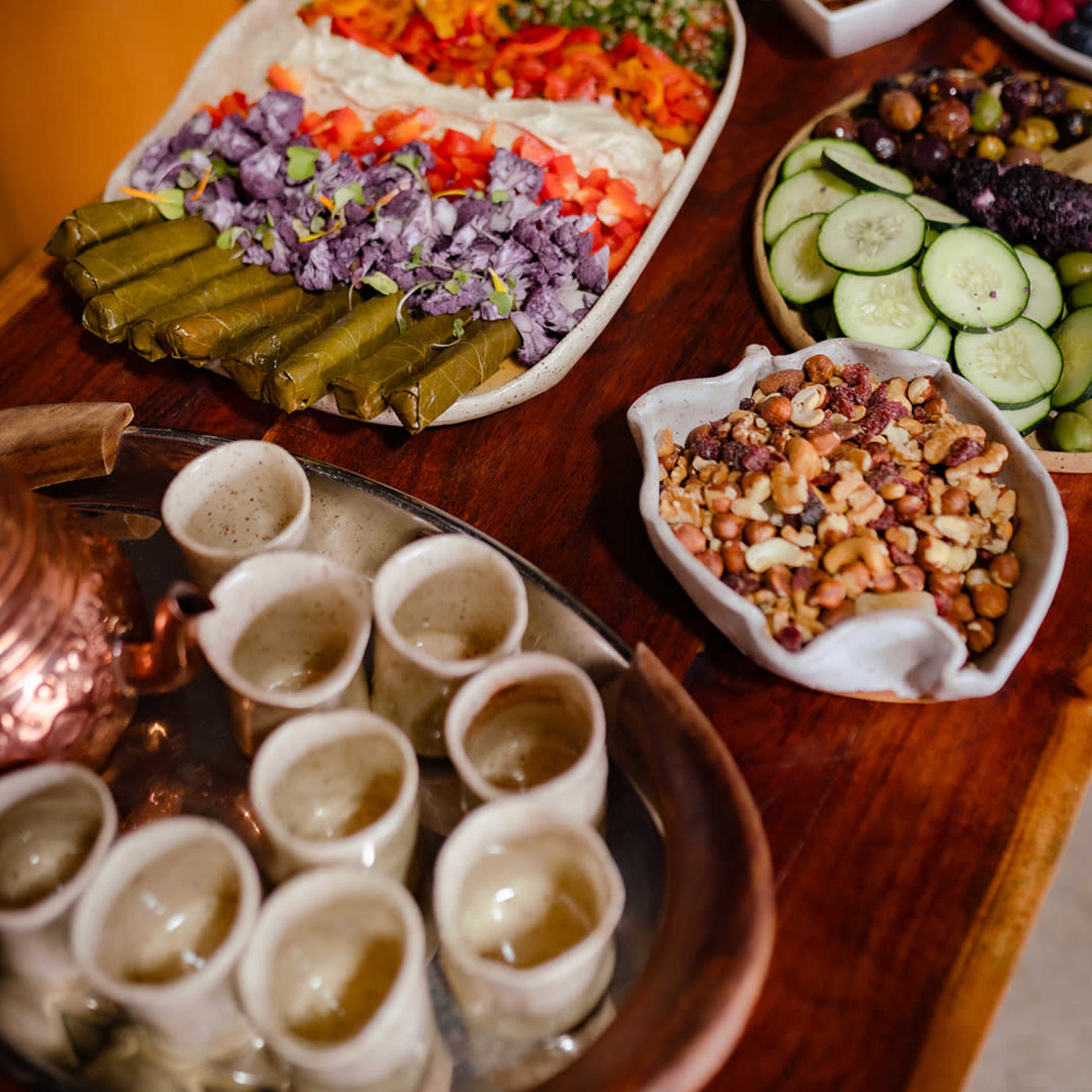 A wooden table displays an assortment of colorful dishes, including stuffed grape leaves, chopped vegetables, and various snacks in bowls.